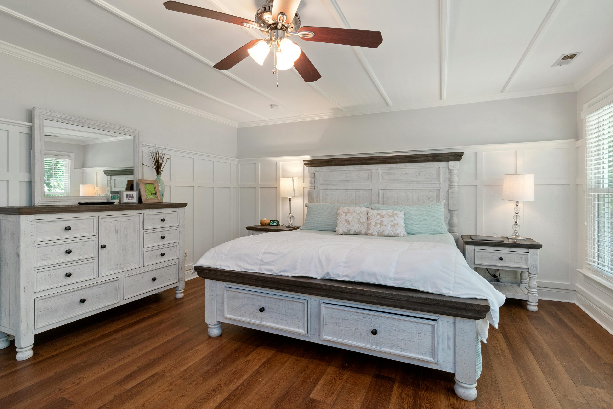 Spacious bedroom featuring a wooden bed, dresser, and ceiling fan with soft lighting.