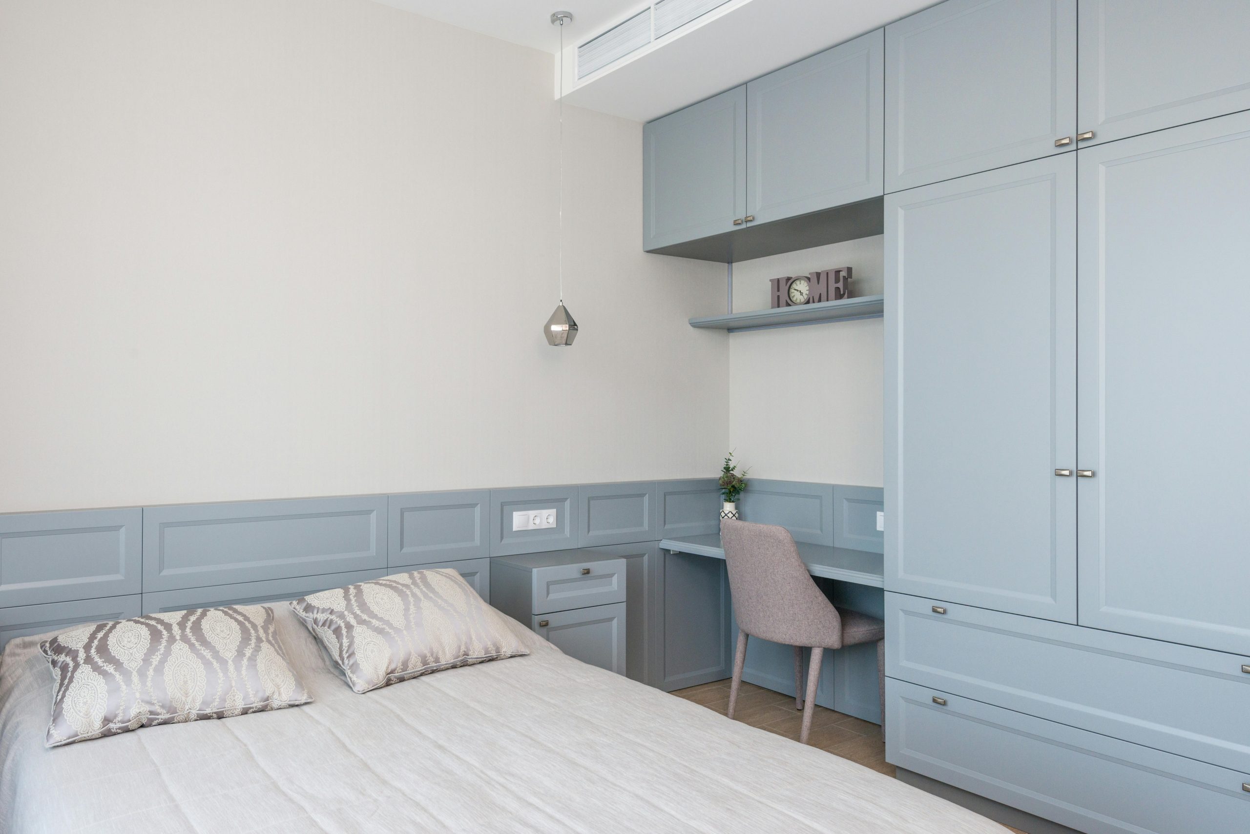 Stylish bedroom features built-in cabinetry, soft blue tones, and a cozy workspace.