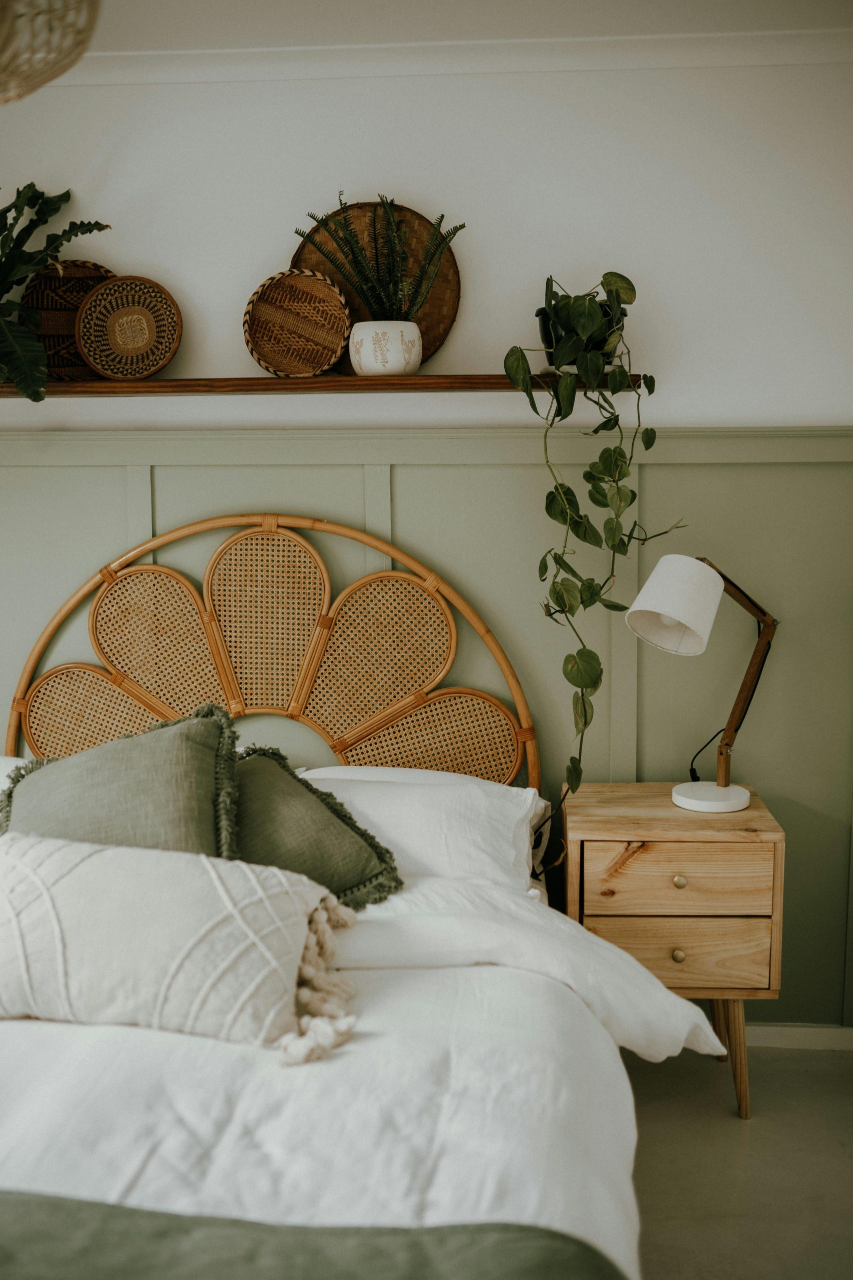 Stylish bedroom with a rattan headboard, green decor, and hanging plants for a serene ambiance.