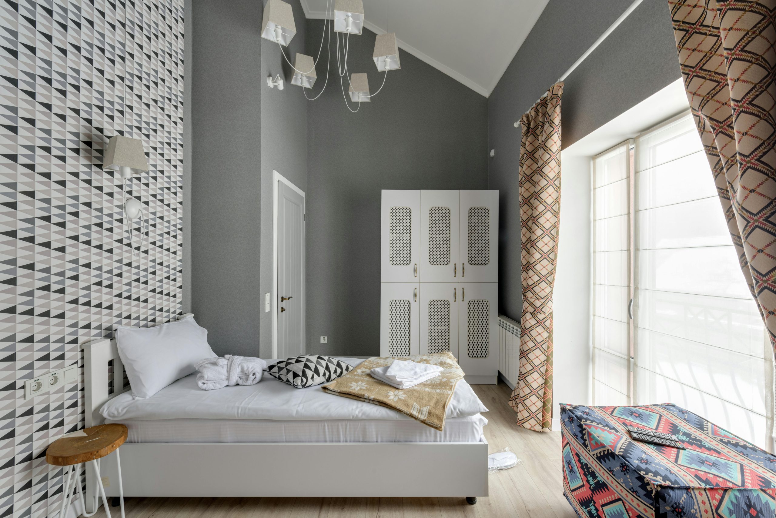 Stylish contemporary bedroom featuring geometric wallpaper, natural light, and chic furnishings.