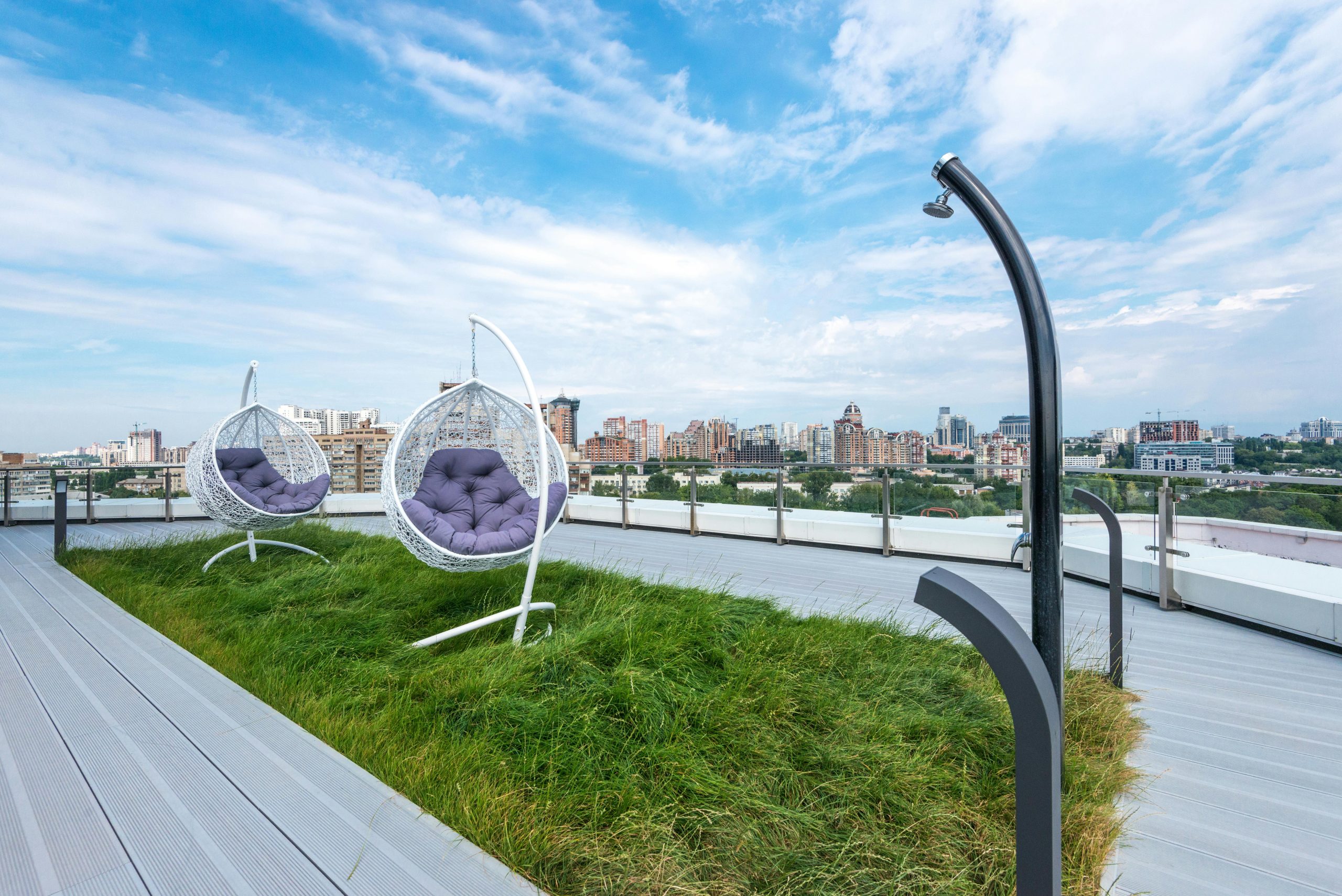 Stylish rooftop terrace featuring hanging chairs with a city skyline view under a blue sky.