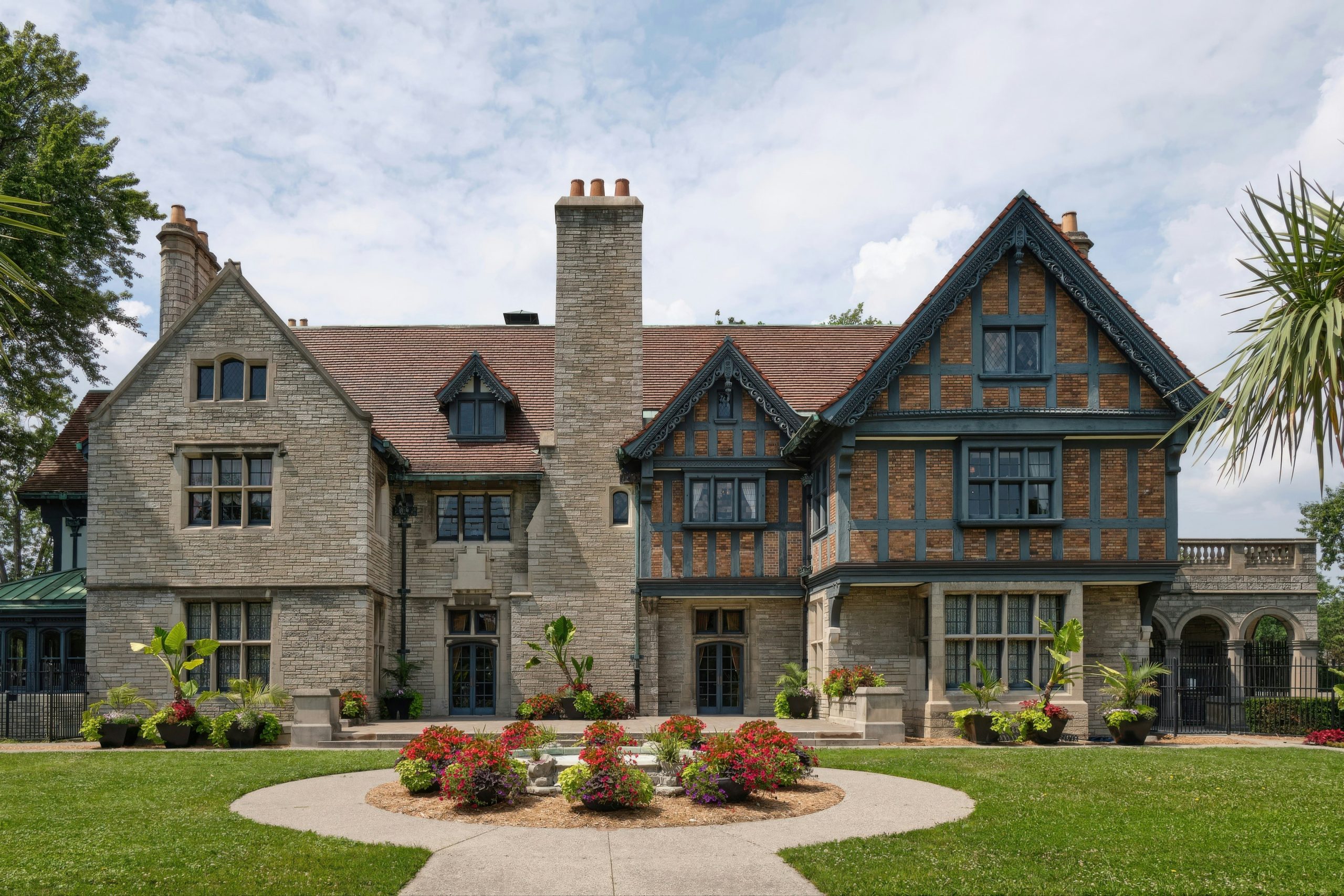 Willistead Manor. Historic stone mansion set in a landscaped garden with manicured lawn, mature trees and architectural details including chimneys, arched windows and terraces conveying elegance and t