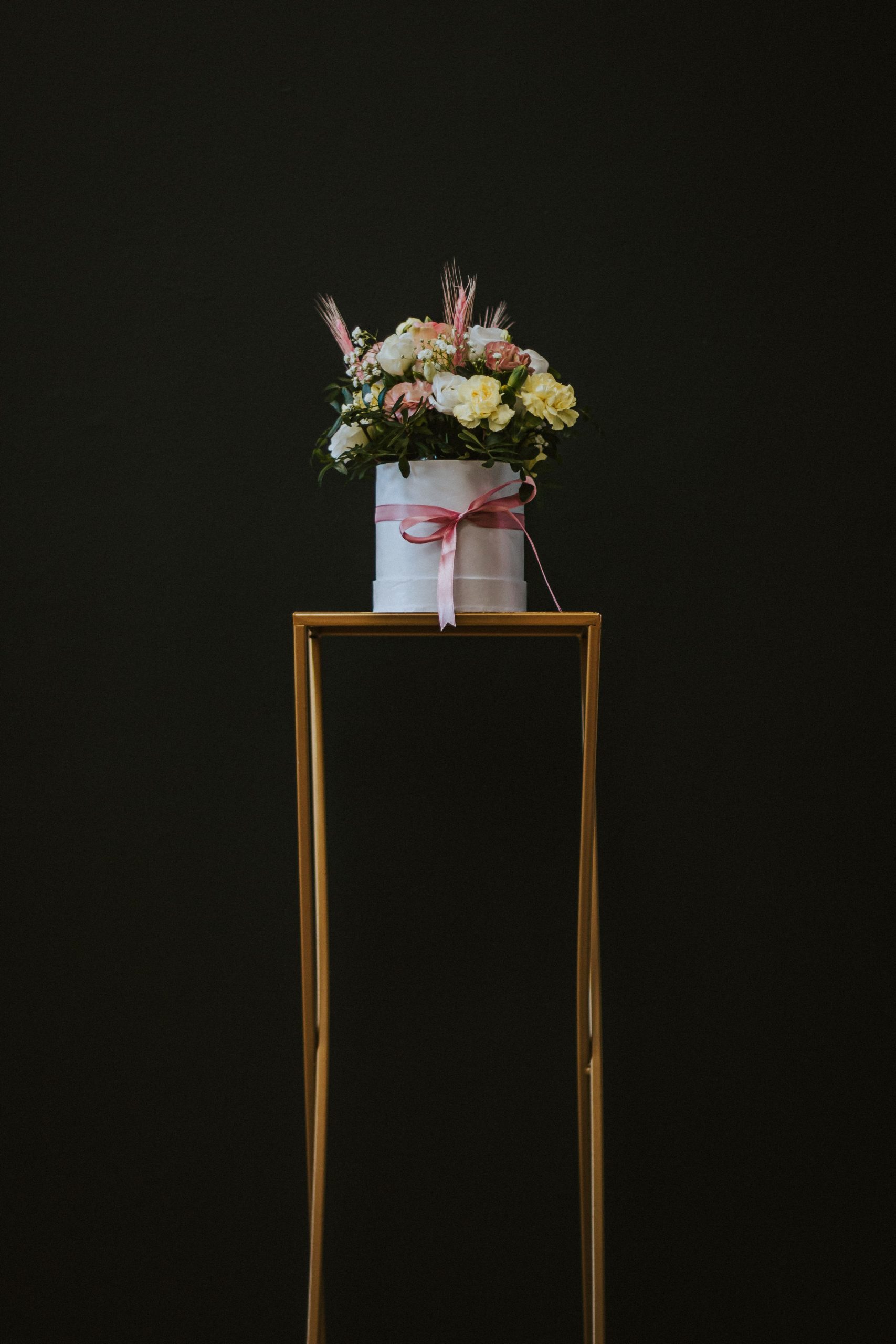 A beautiful bouquet of flowers in a decorative container on a minimalist stand against a dark background.