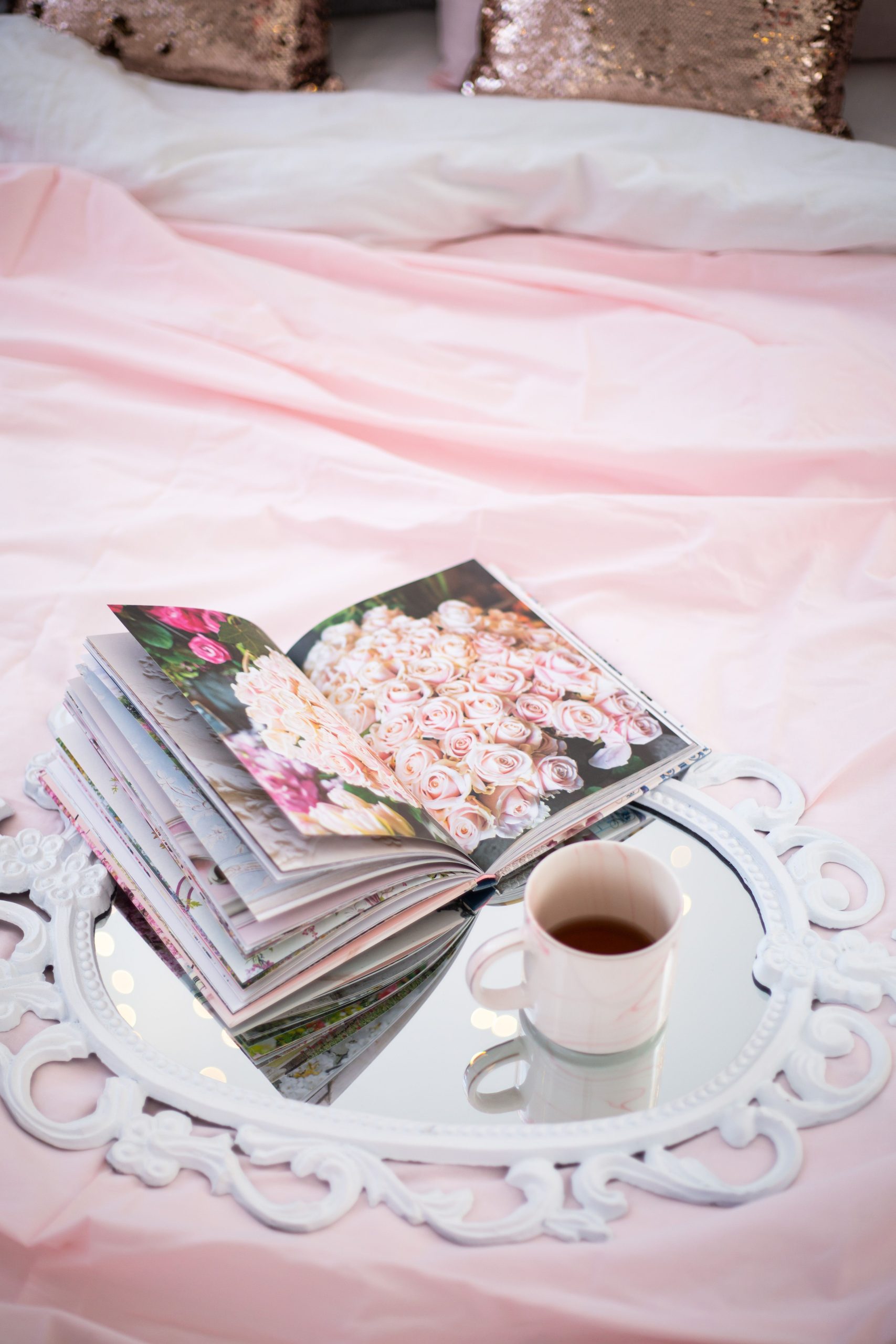 A charming scene of a book and tea on an ornate mirror in a soft pink bedroom.