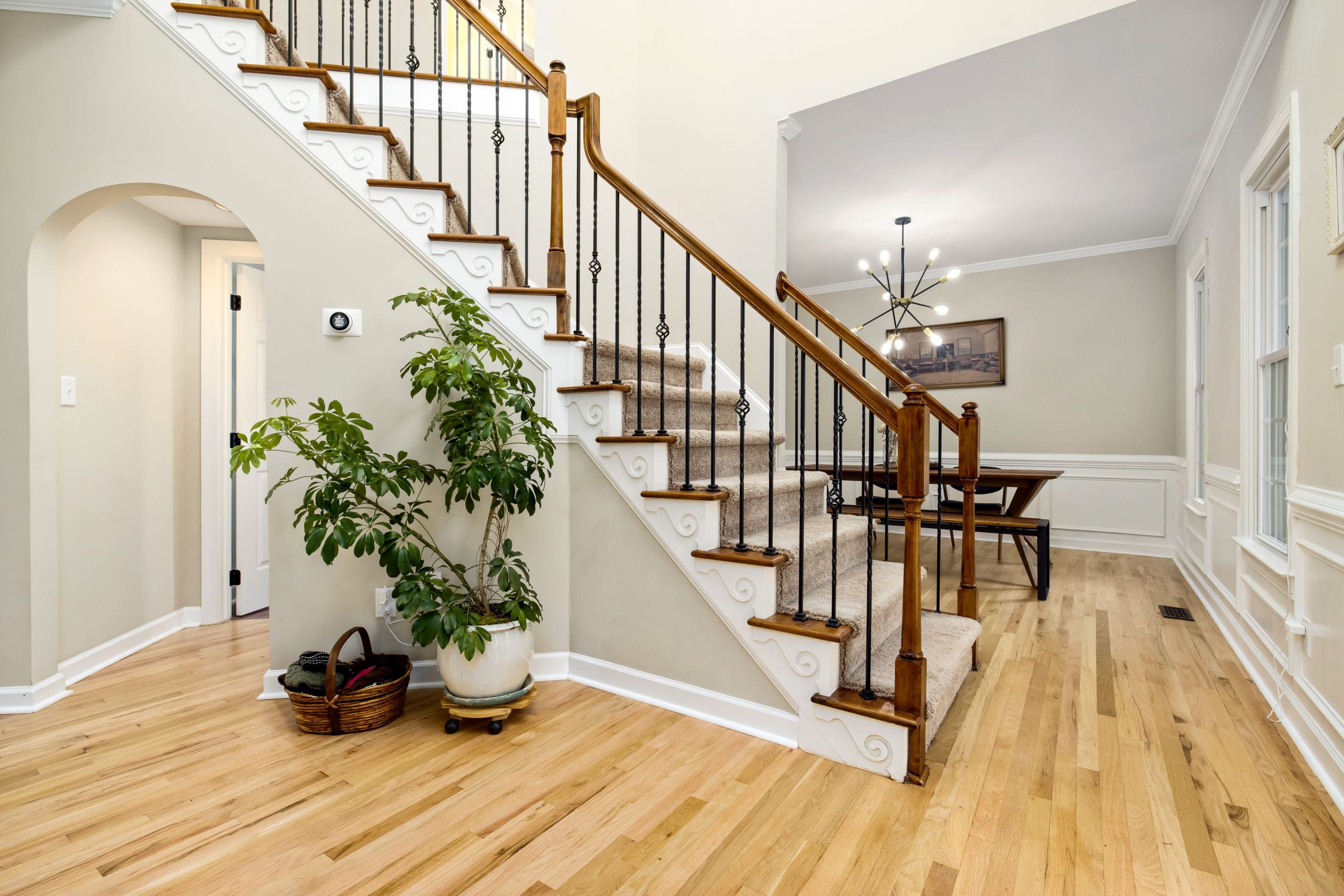 A chic and spacious interior featuring a wooden staircase with wrought iron railing and potted greenery.