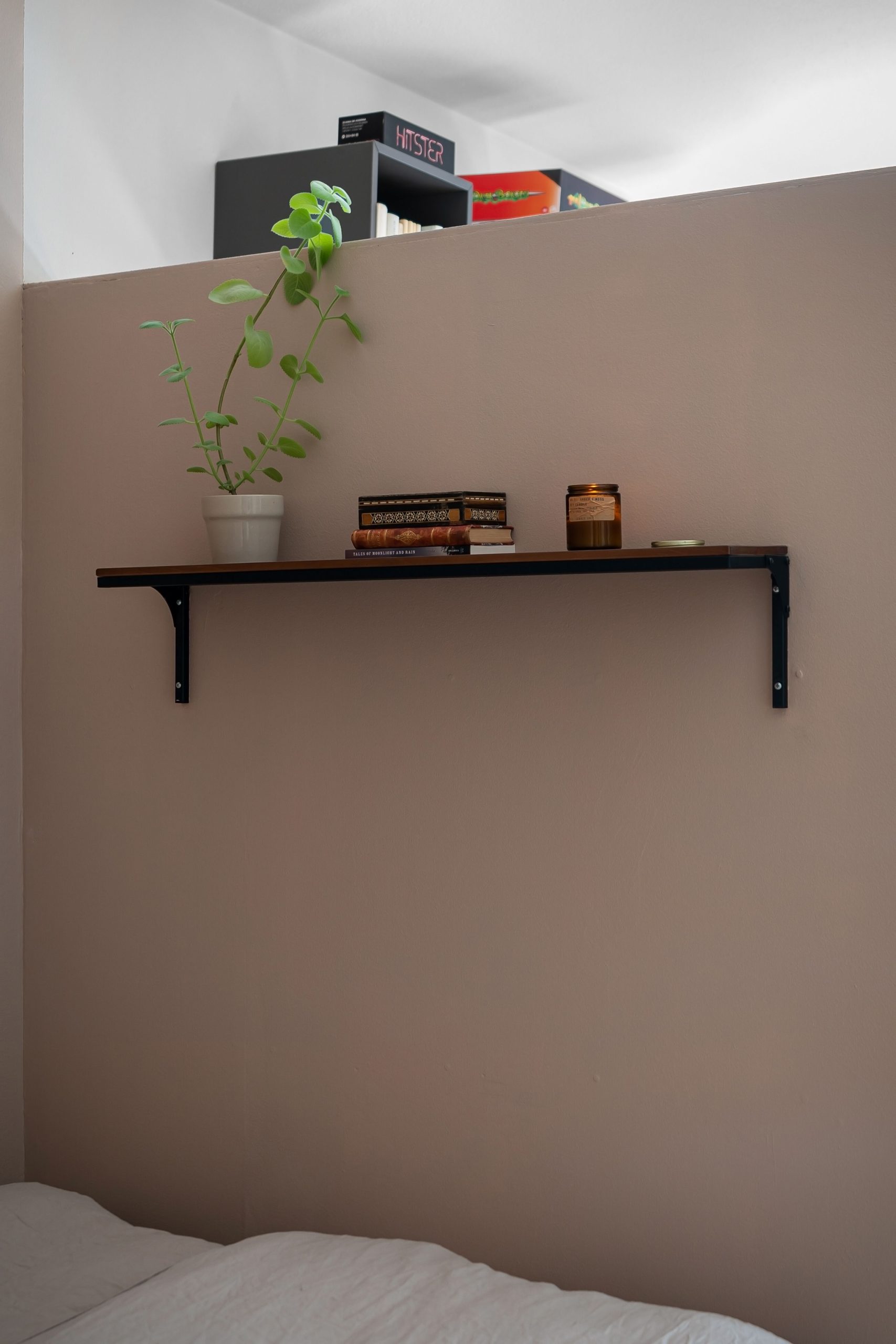 A minimalist bedroom featuring a wall shelf with books, a plant, and a candle for a cozy atmosphere.