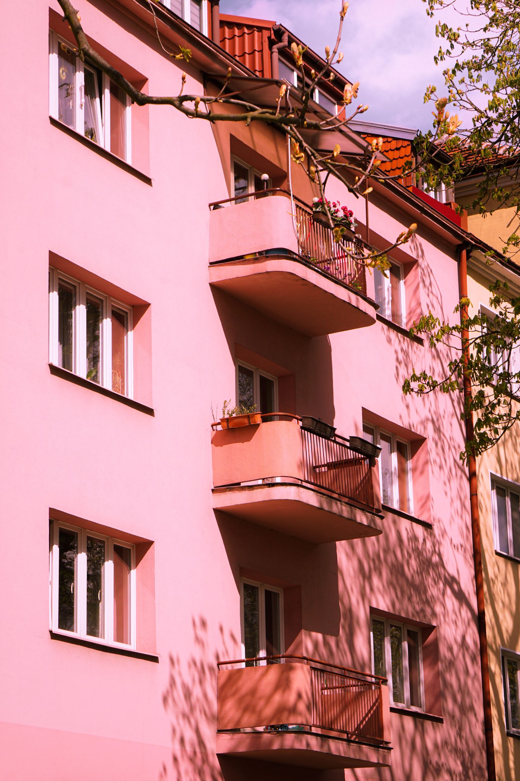 A pastel pink apartment building exterior with balconies, captured under clear daylight, showcasing an urban residential area.