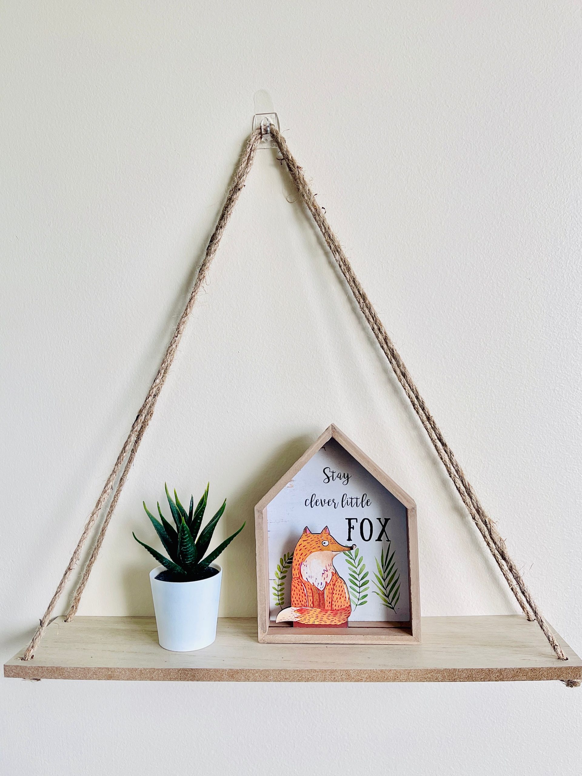 A rustic wooden shelf with a tiny plant and decorative fox art enhances minimalistic home decor.