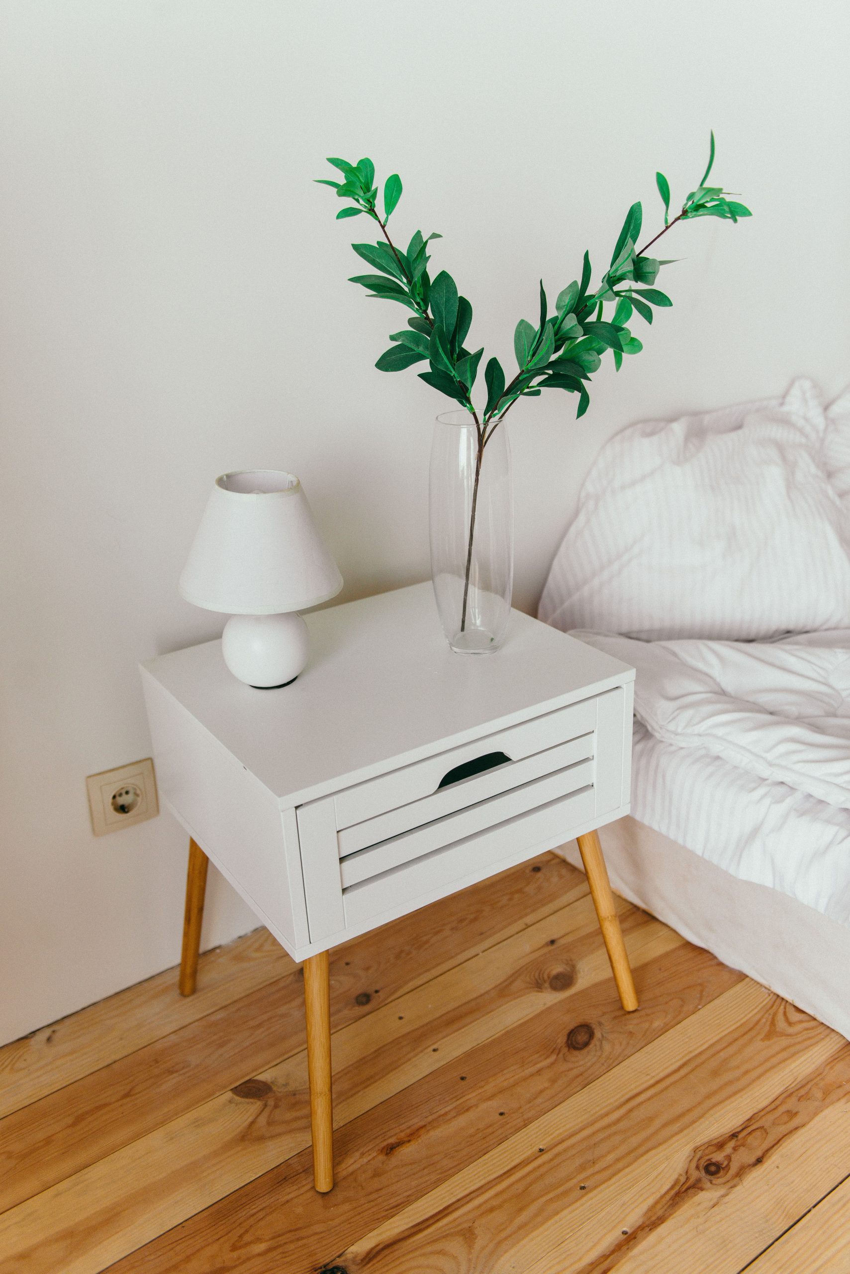 A stylish bedroom showcasing a white nightstand with a vase and lamp, perfect for modern interior design inspiration.