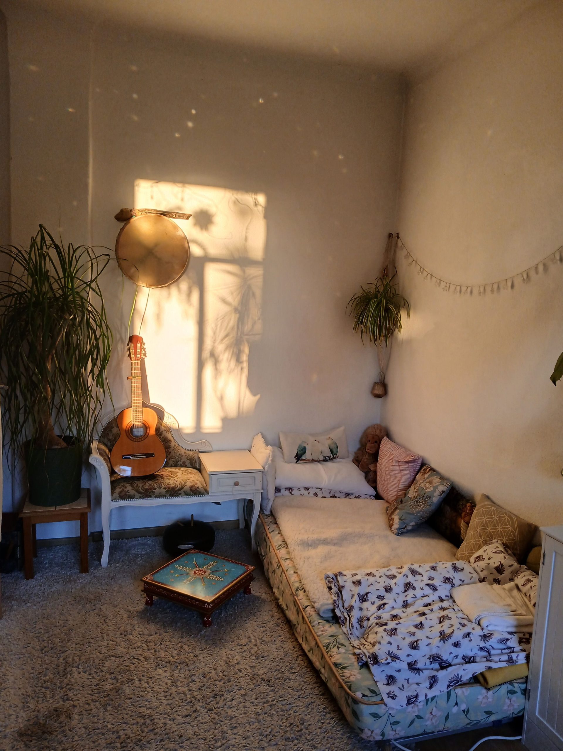 A warm, inviting room with bohemian decor and sunlight, featuring a guitar and plants.