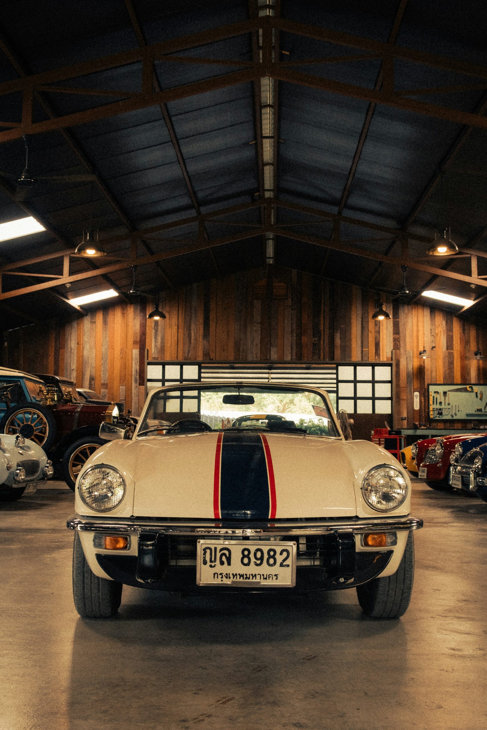 A white vintage car with racing stripes in a garage.
