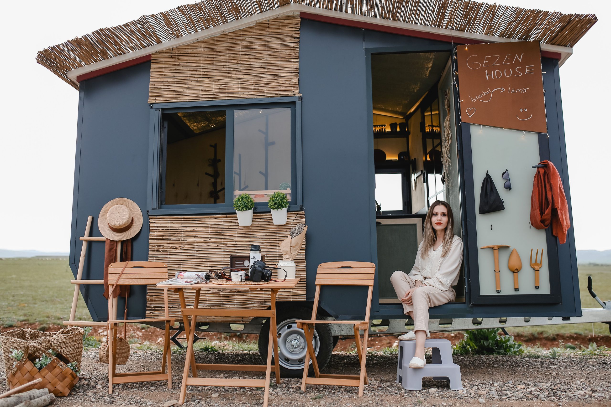 A woman relaxing outside her modern tiny mobile home in a scenic outdoor setting.