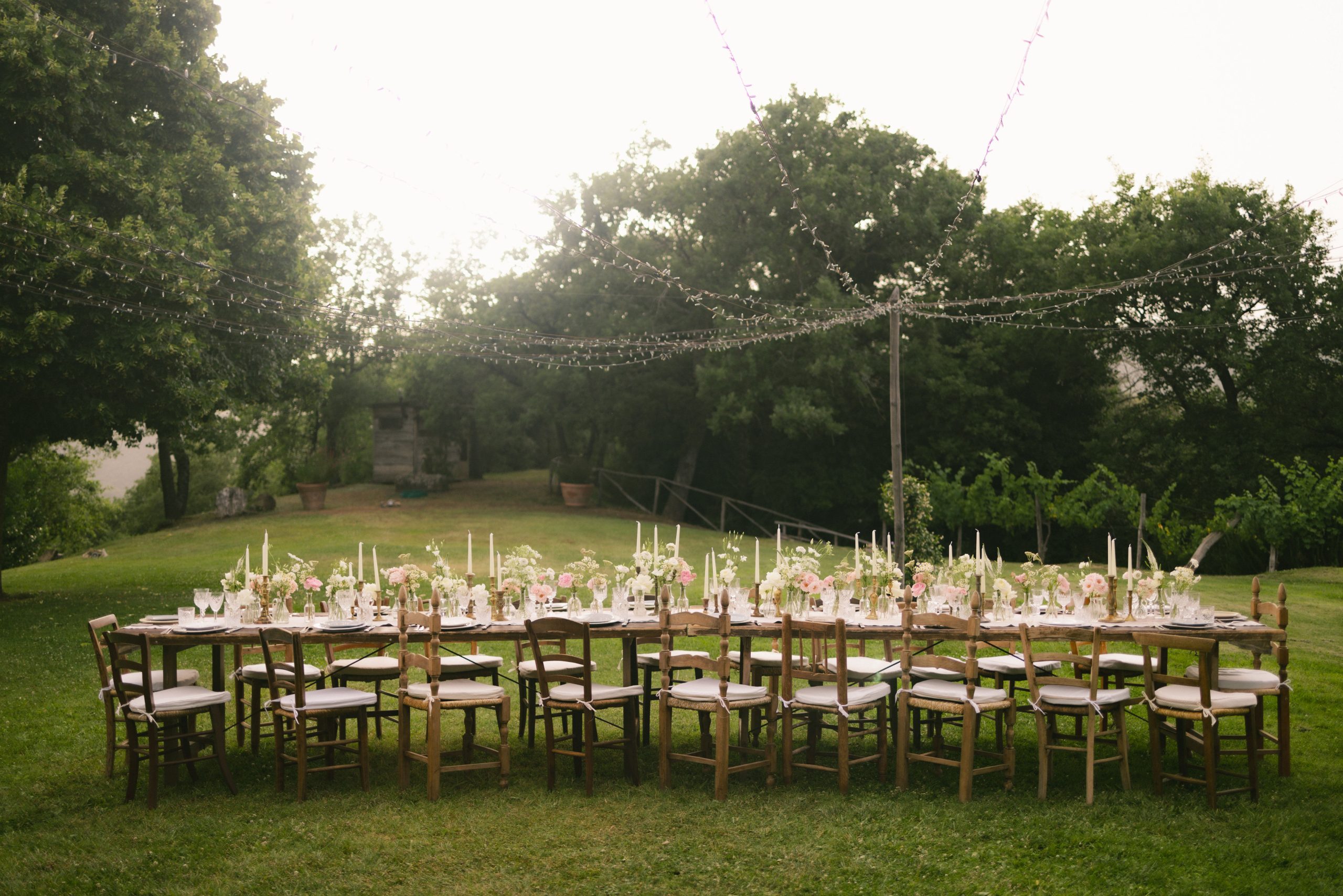 Beautiful outdoor wedding reception table setup with floral decorations and string lights in a garden.