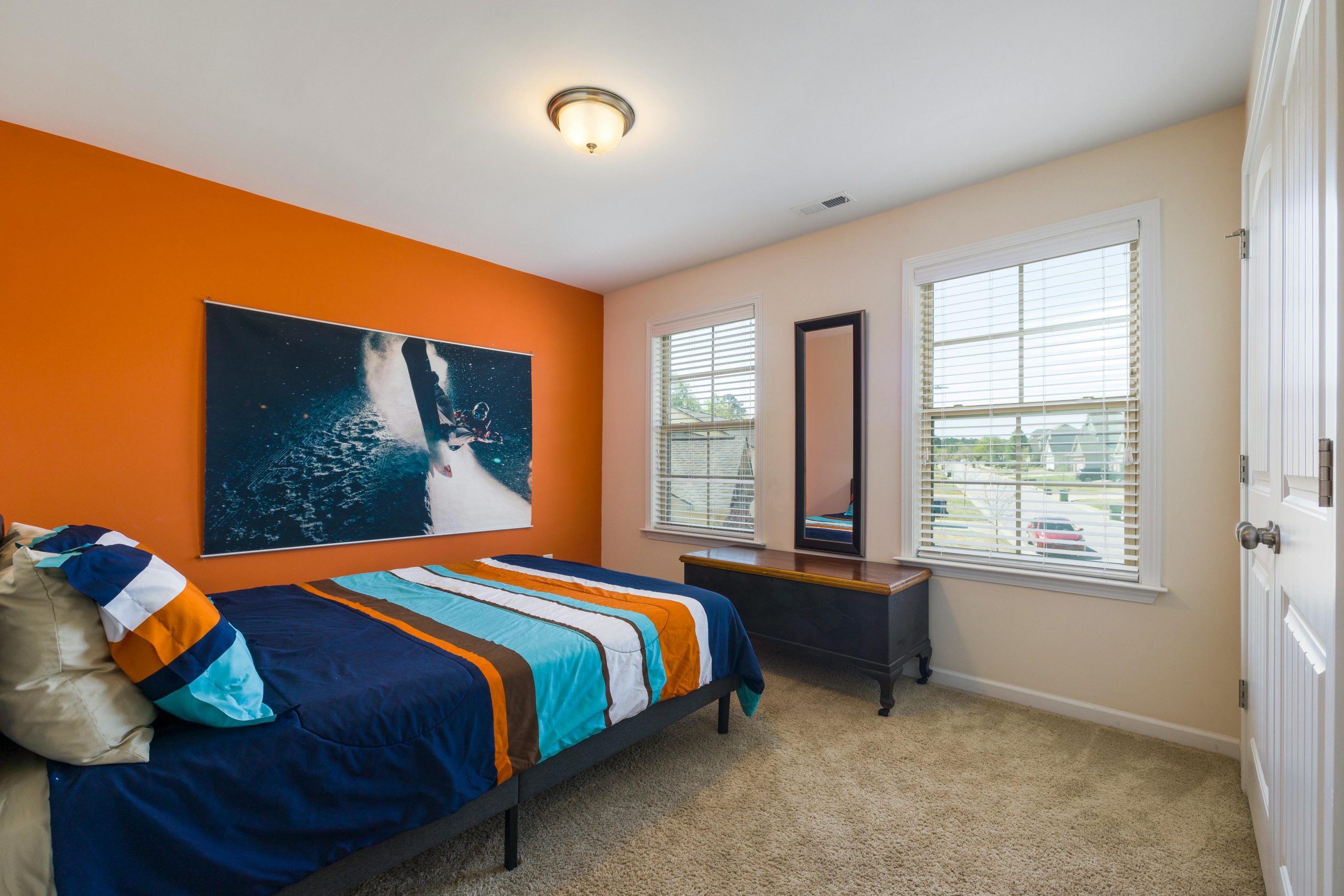 Bright bedroom featuring an orange accent wall, stylish bedding, and large windows.