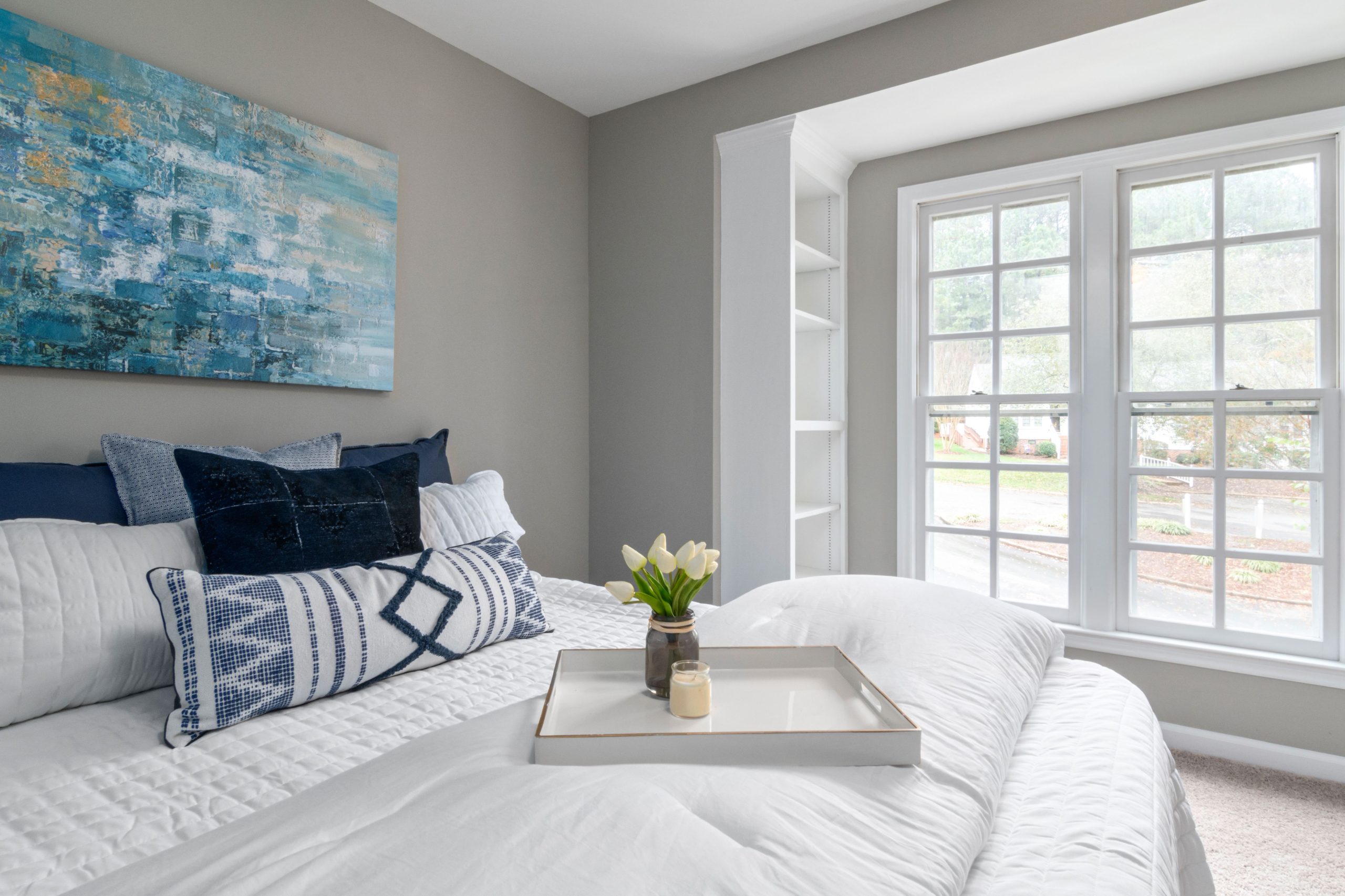 Bright minimalist bedroom with a cozy bed, blue decor, and natural light from large windows.