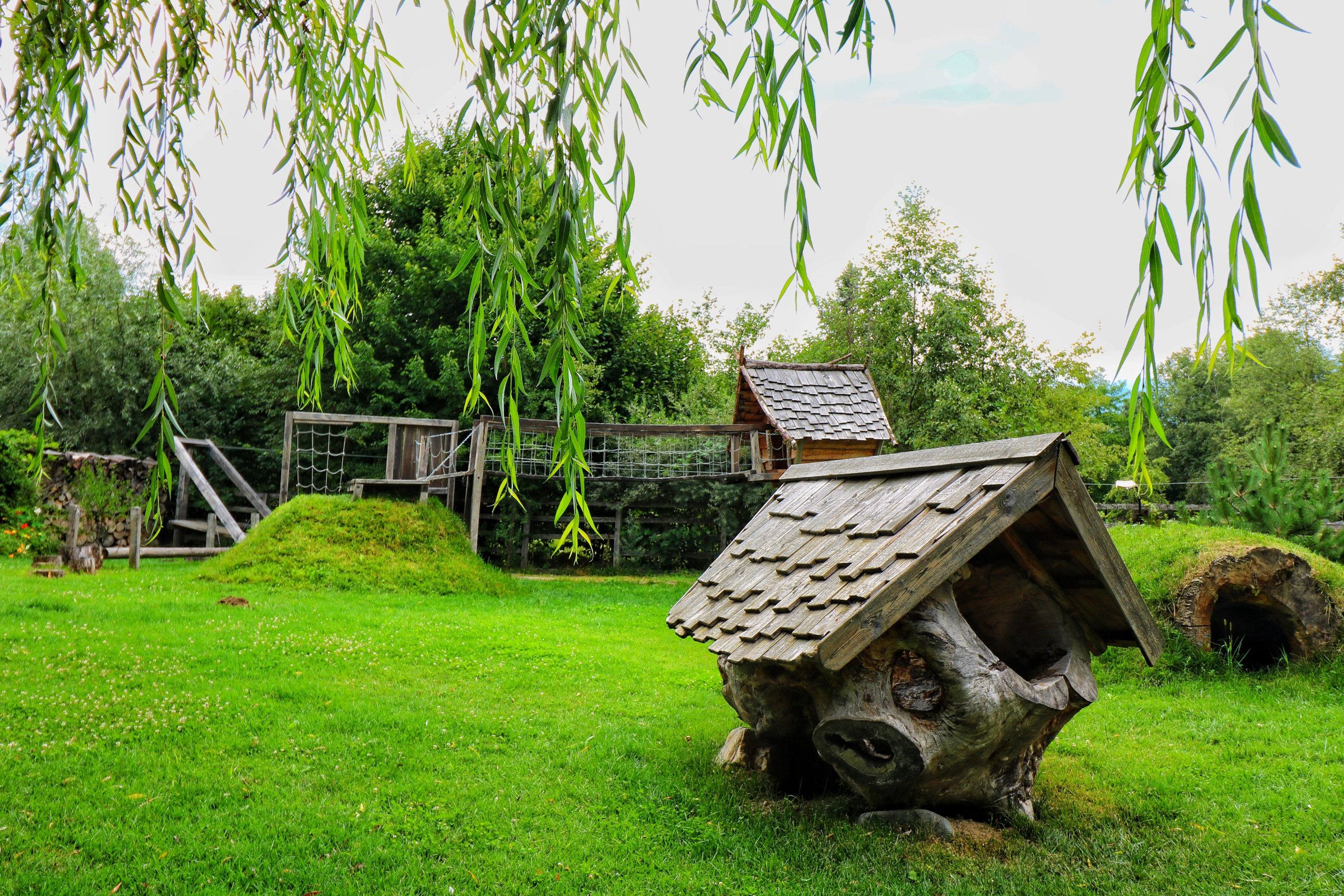 Charming rustic playground with wooden structures surrounded by lush greenery.