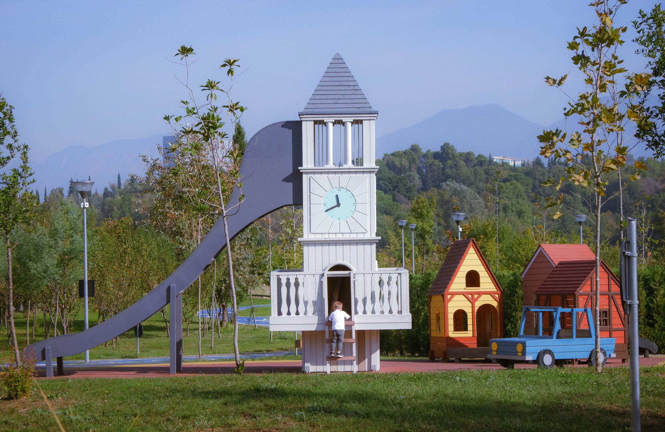 Child exploring whimsical clock tower slide in a scenic park.