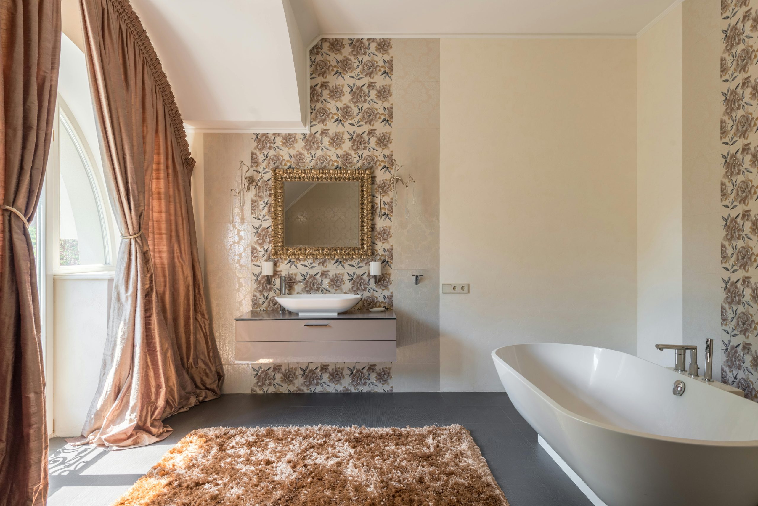Classic bathroom with white clean oval shaped bathtub with tap near window with brown curtains