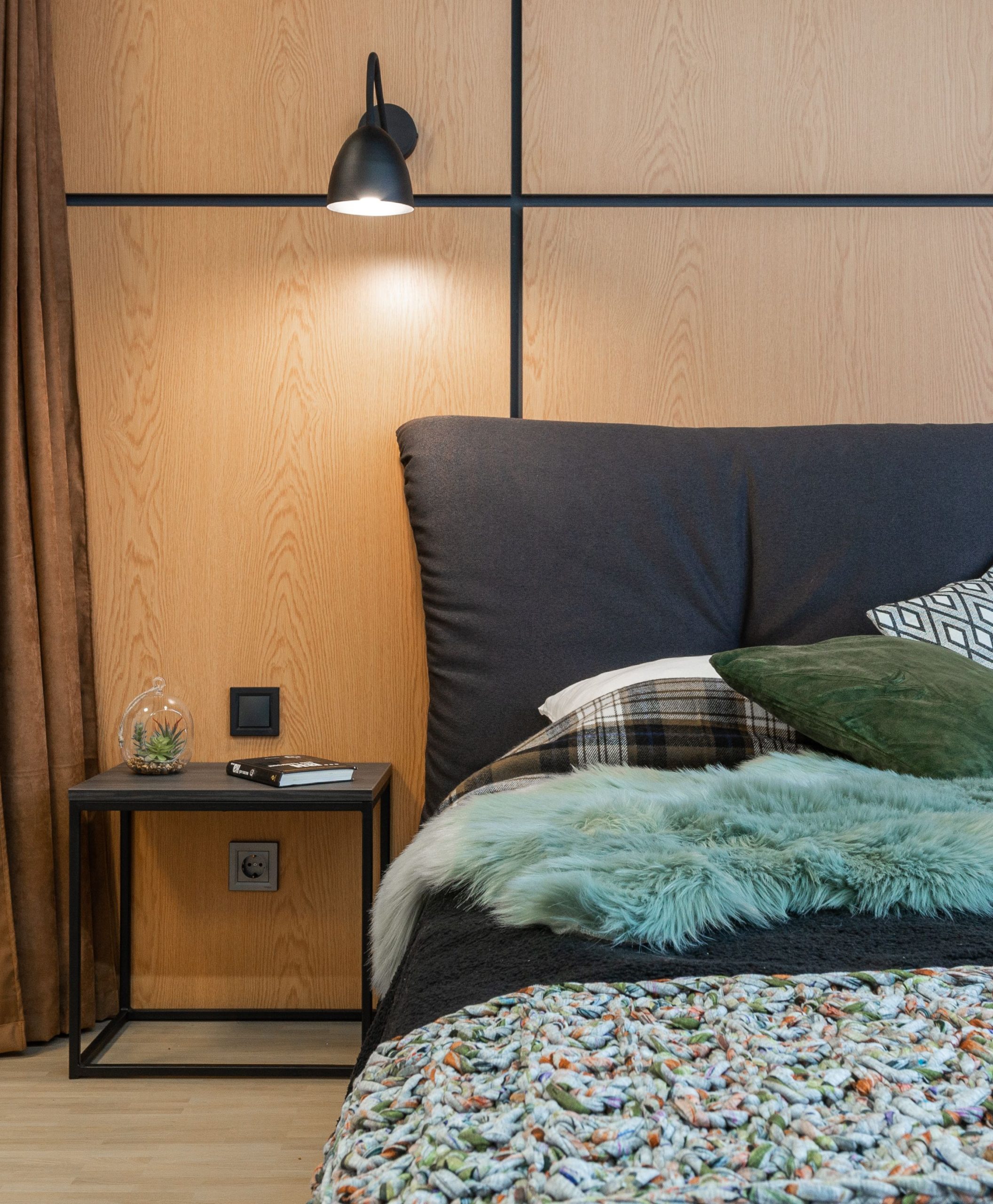 Comfortable bed with pillows and soft blanket placed at wooden wall near bedside table in modern light bedroom at home