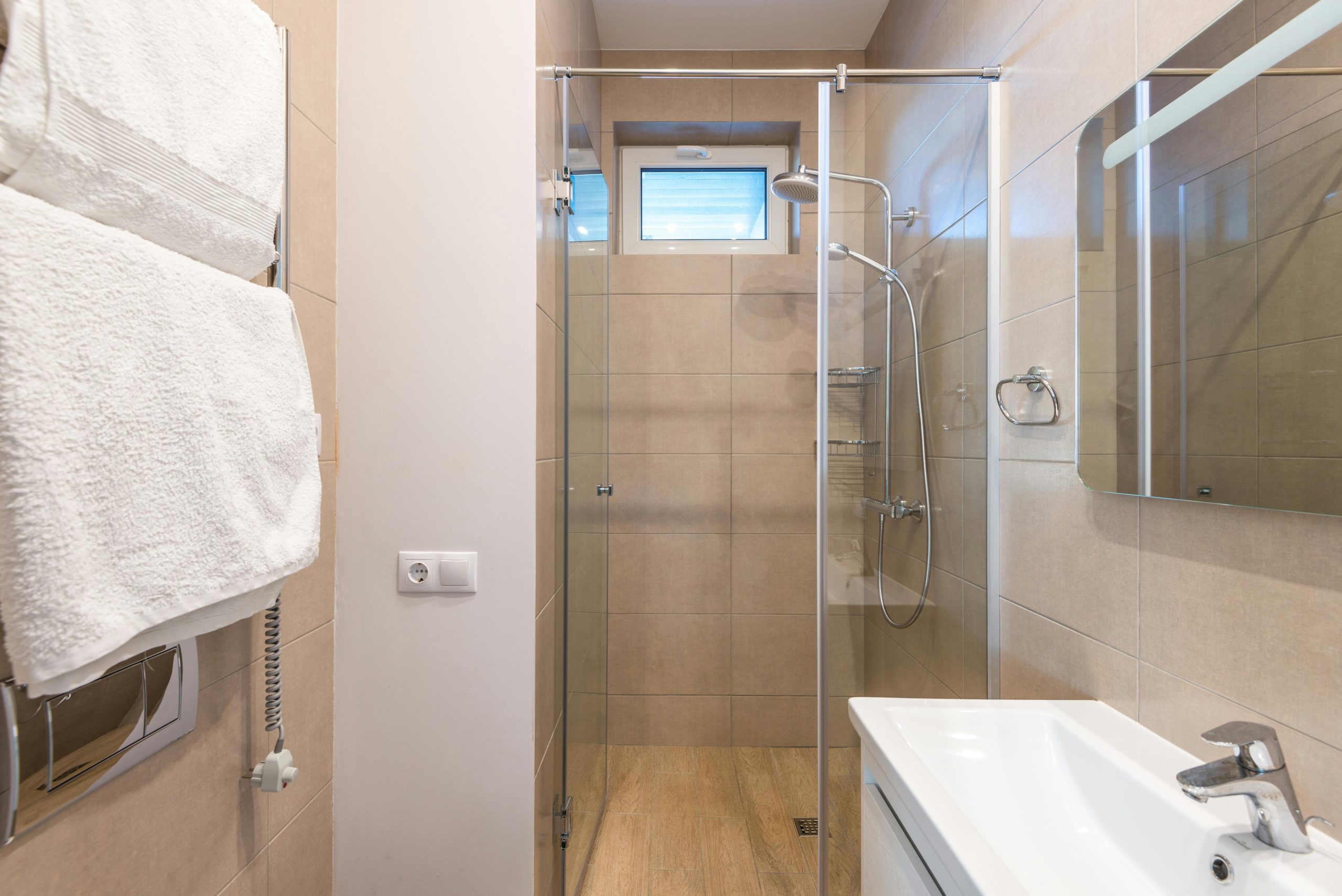 Contemporary bathroom featuring a glass shower, beige tiles, and a sleek sink area.