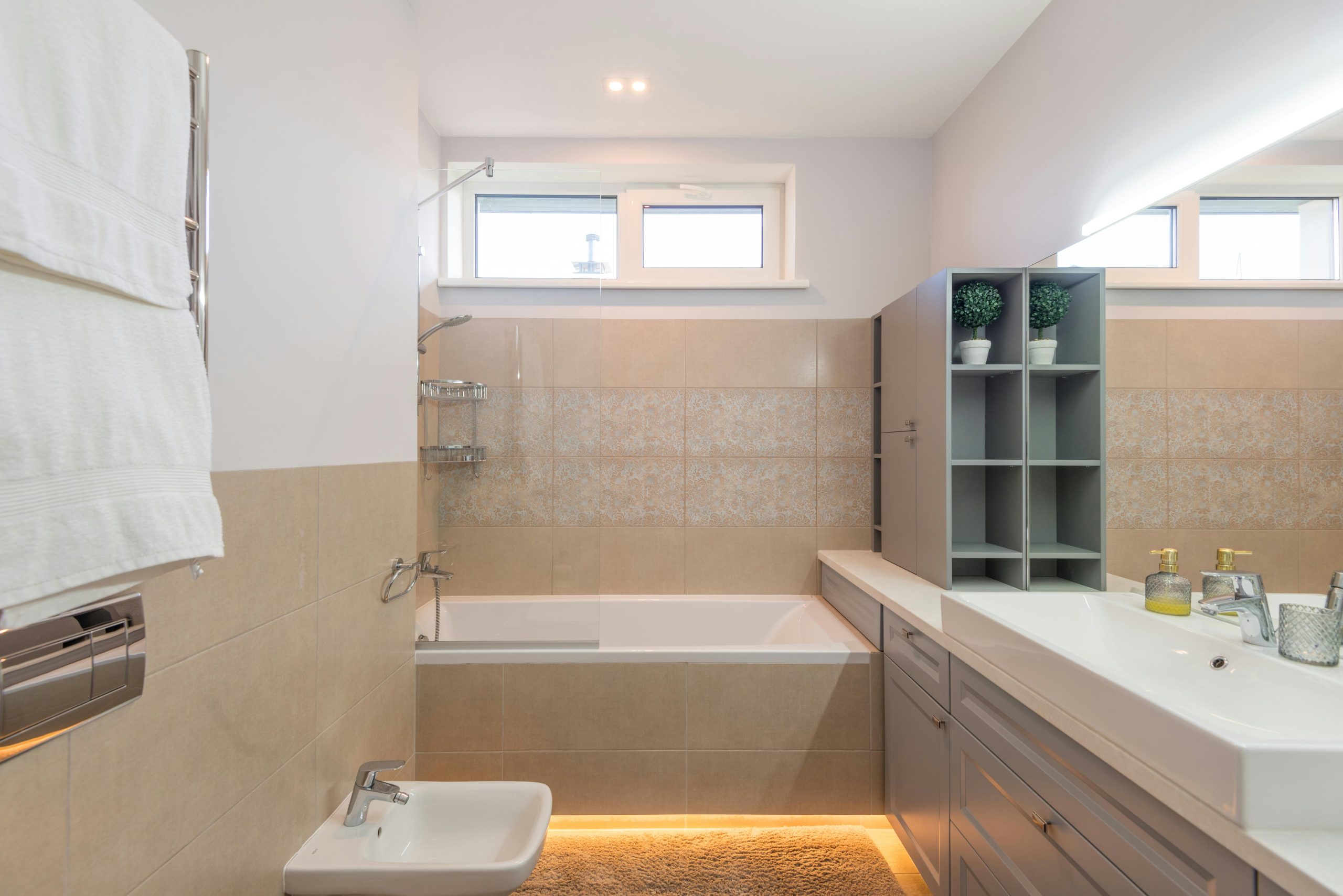 Contemporary beige bathroom featuring a bathtub, sink, and stylish mirror with ample lighting.