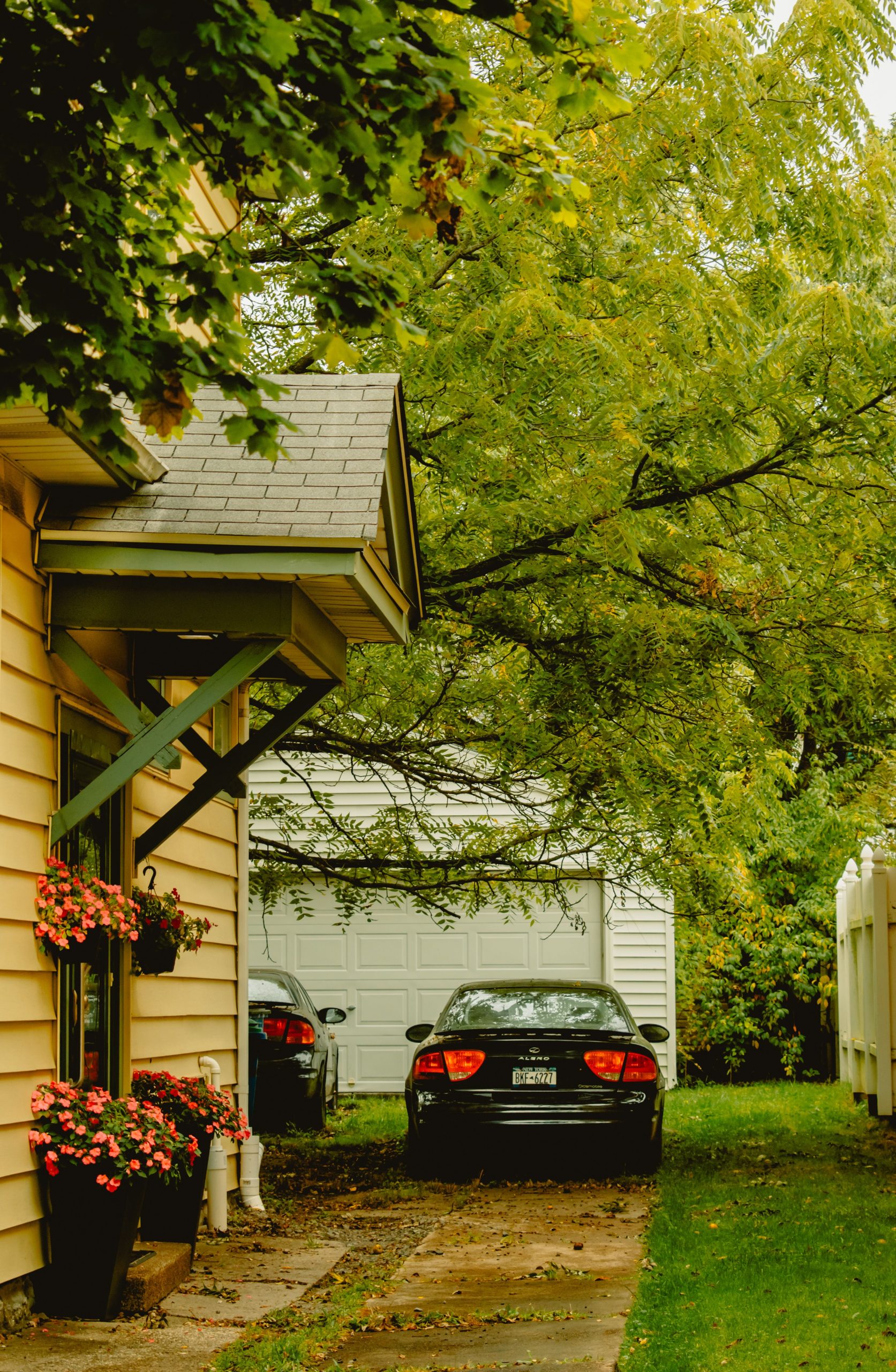 Cozy suburban setting featuring a house with colorful flowers and cars parked beside a garage under lush trees.