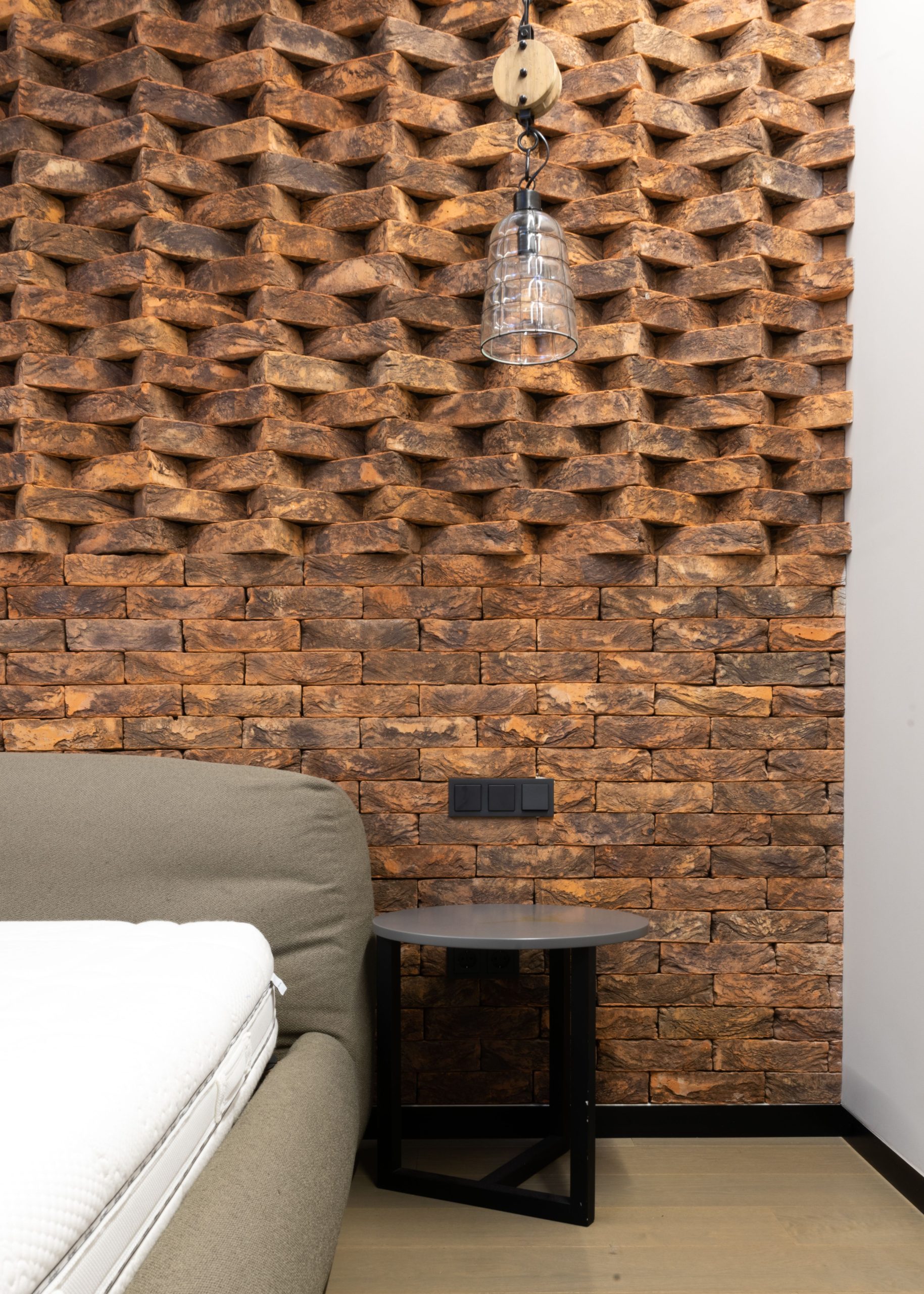 Creative masonry of brick wall in modern loft style bedroom with glass lamp hanging over small table placed near comfortable bed