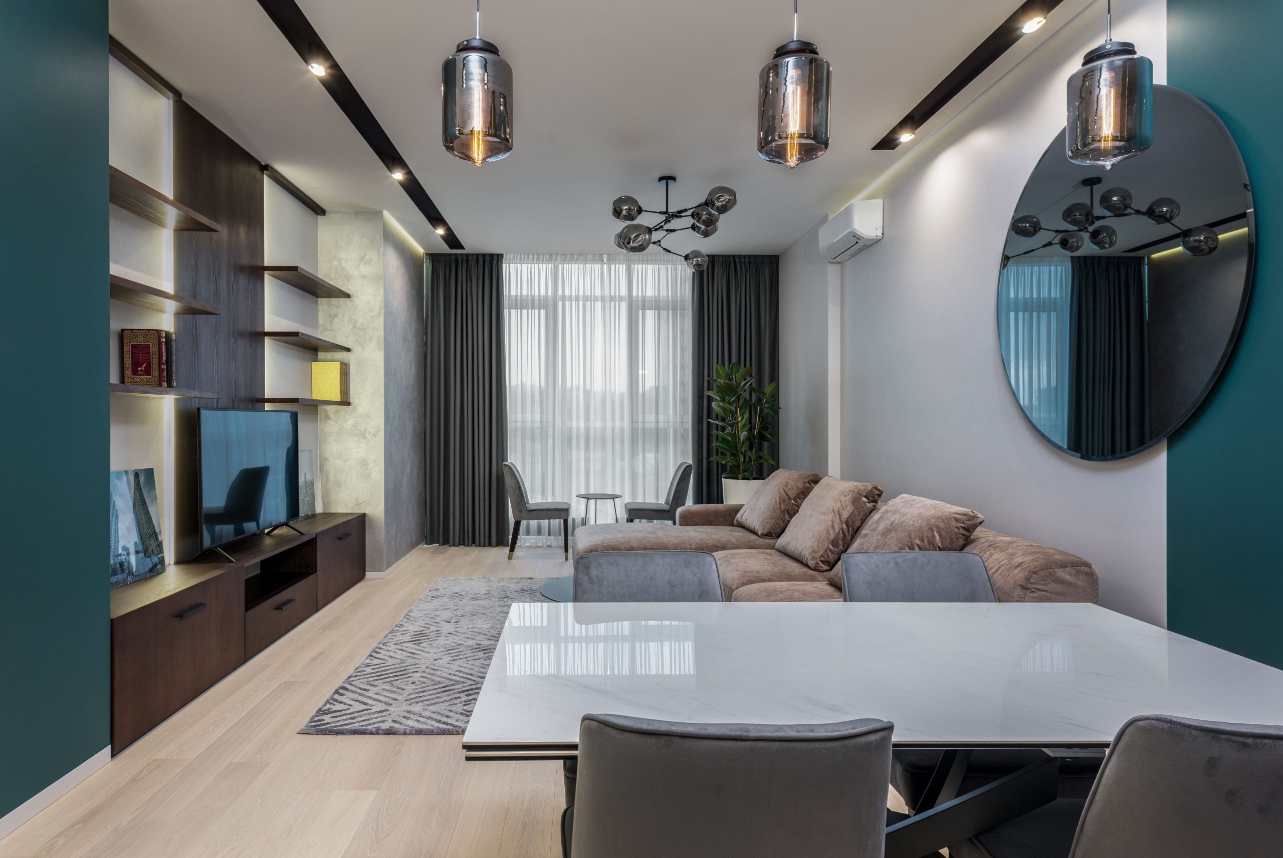 Dining table with chairs placed near comfortable couch and modern TV set in cozy living room decorated with mirror and lamps