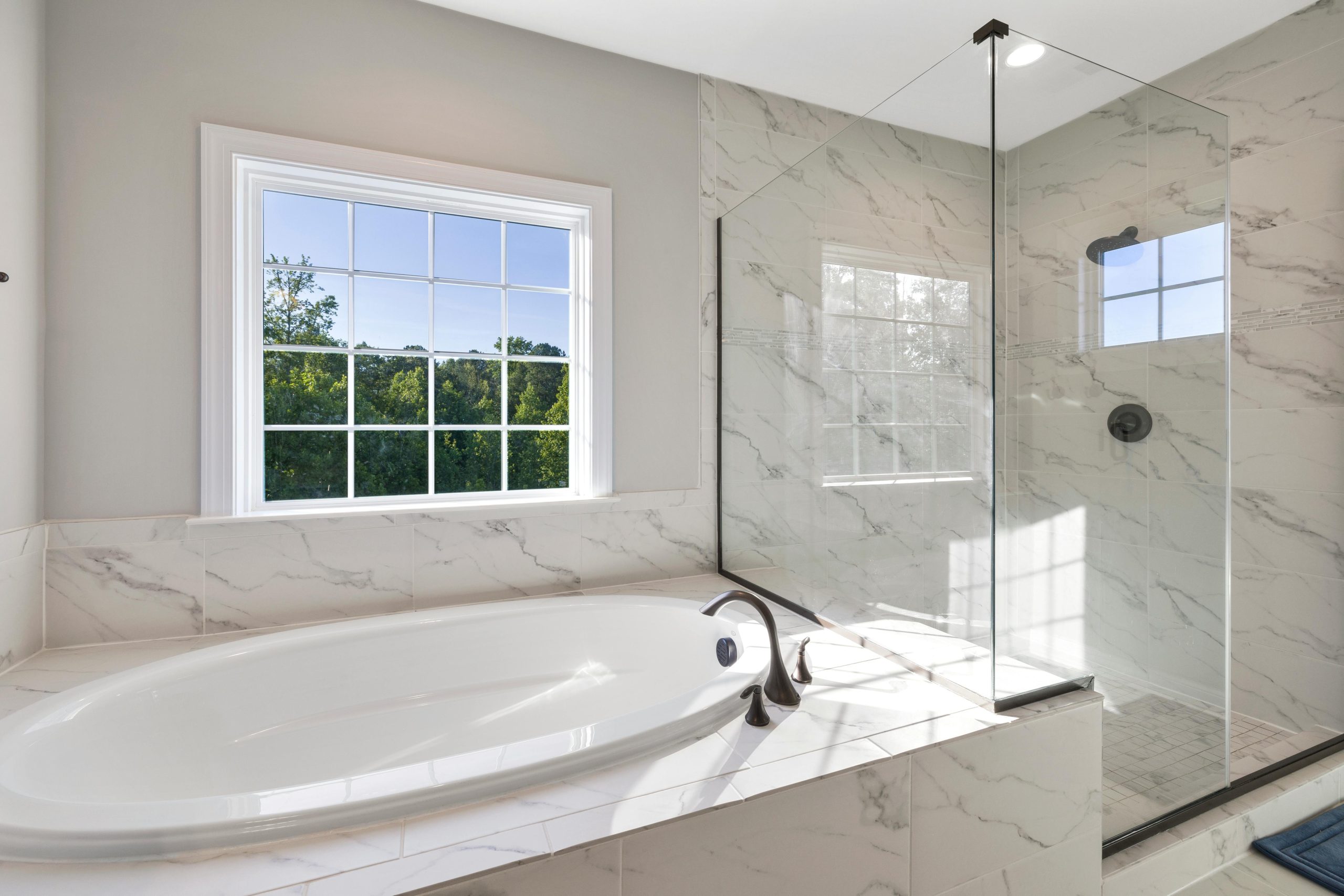 Elegant contemporary bathroom with marble finishes, featuring a sleek bathtub and glass shower.