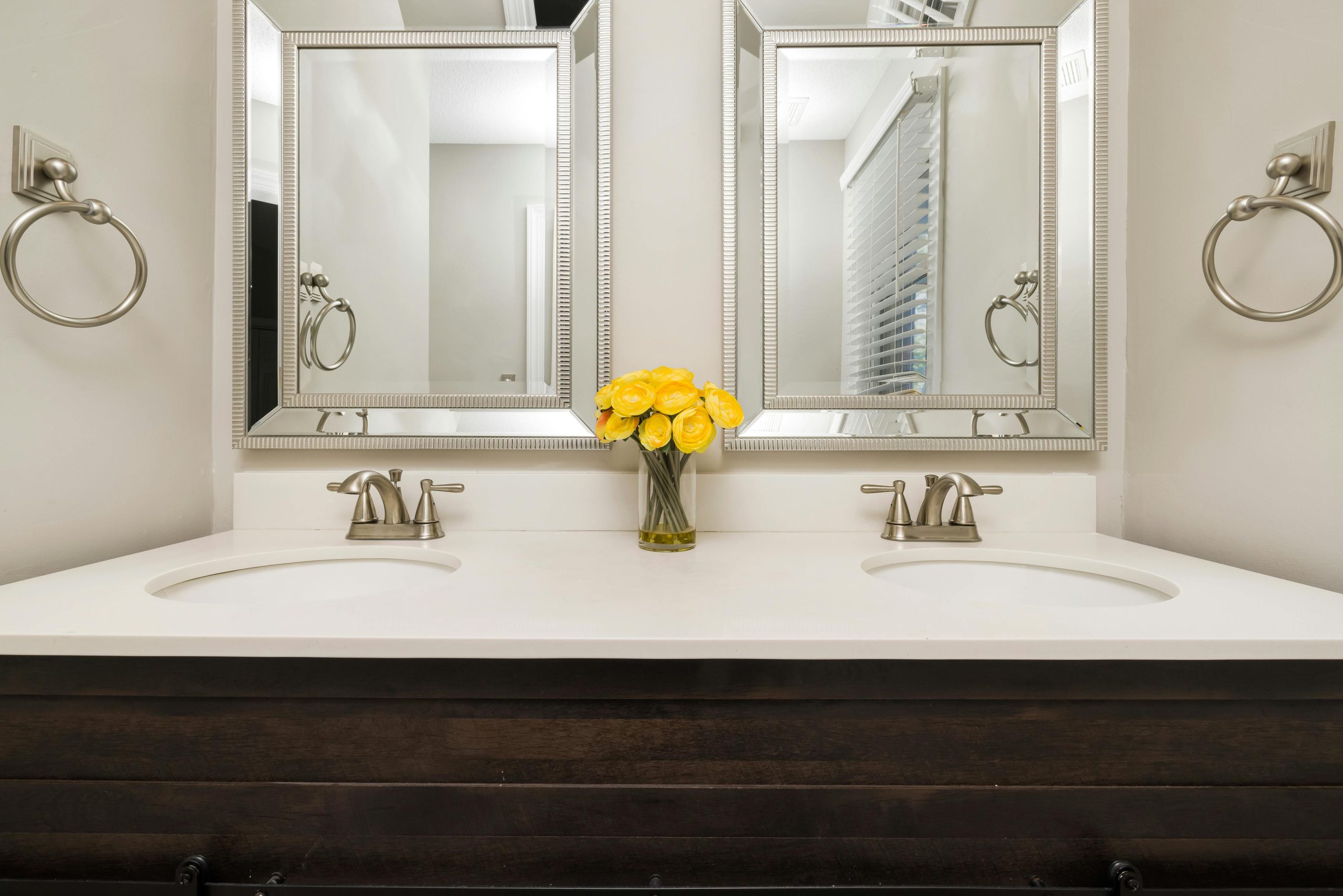 Elegant modern bathroom with twin mirrors, stylish faucets, and a touch of luxury with yellow flowers.
