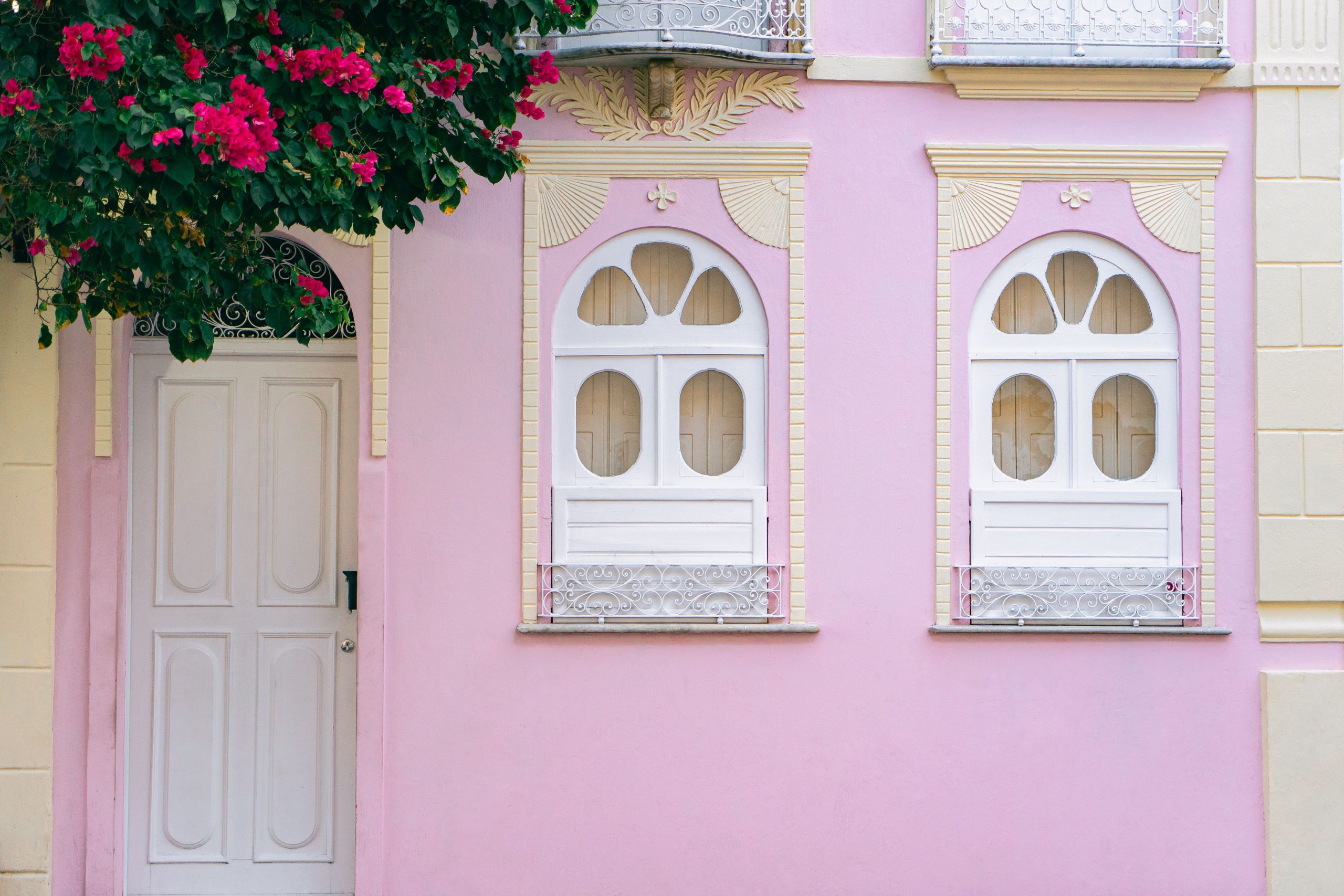 Elegant pink building facade featuring decorative white windows and vibrant bougainvillea.