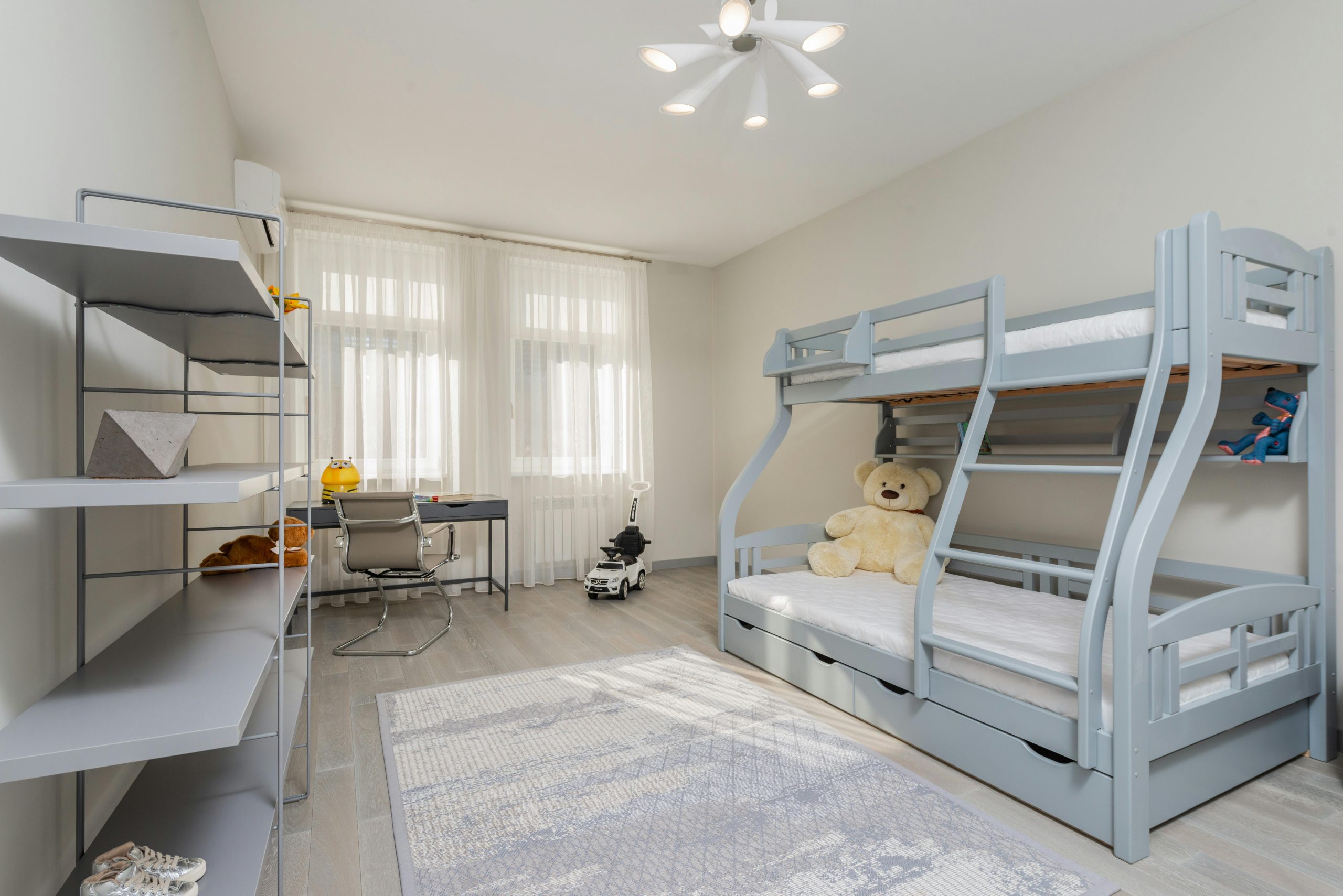 Interior of bedroom with desk and chair near window and gray double deck bed in front of empty shelves
