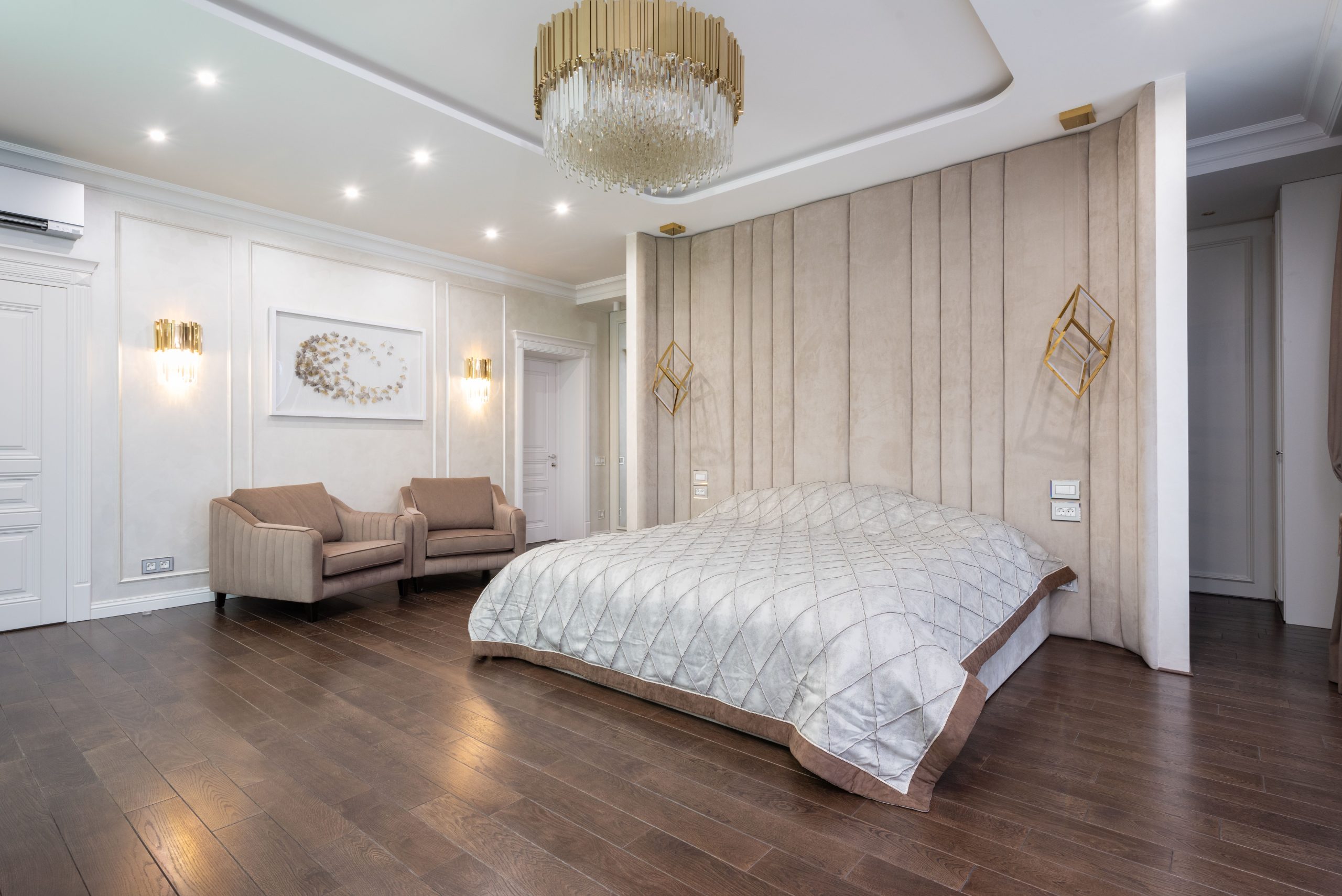 Interior of luxury bedroom with parquet flooring and big bed under chandelier next to armchairs and doors