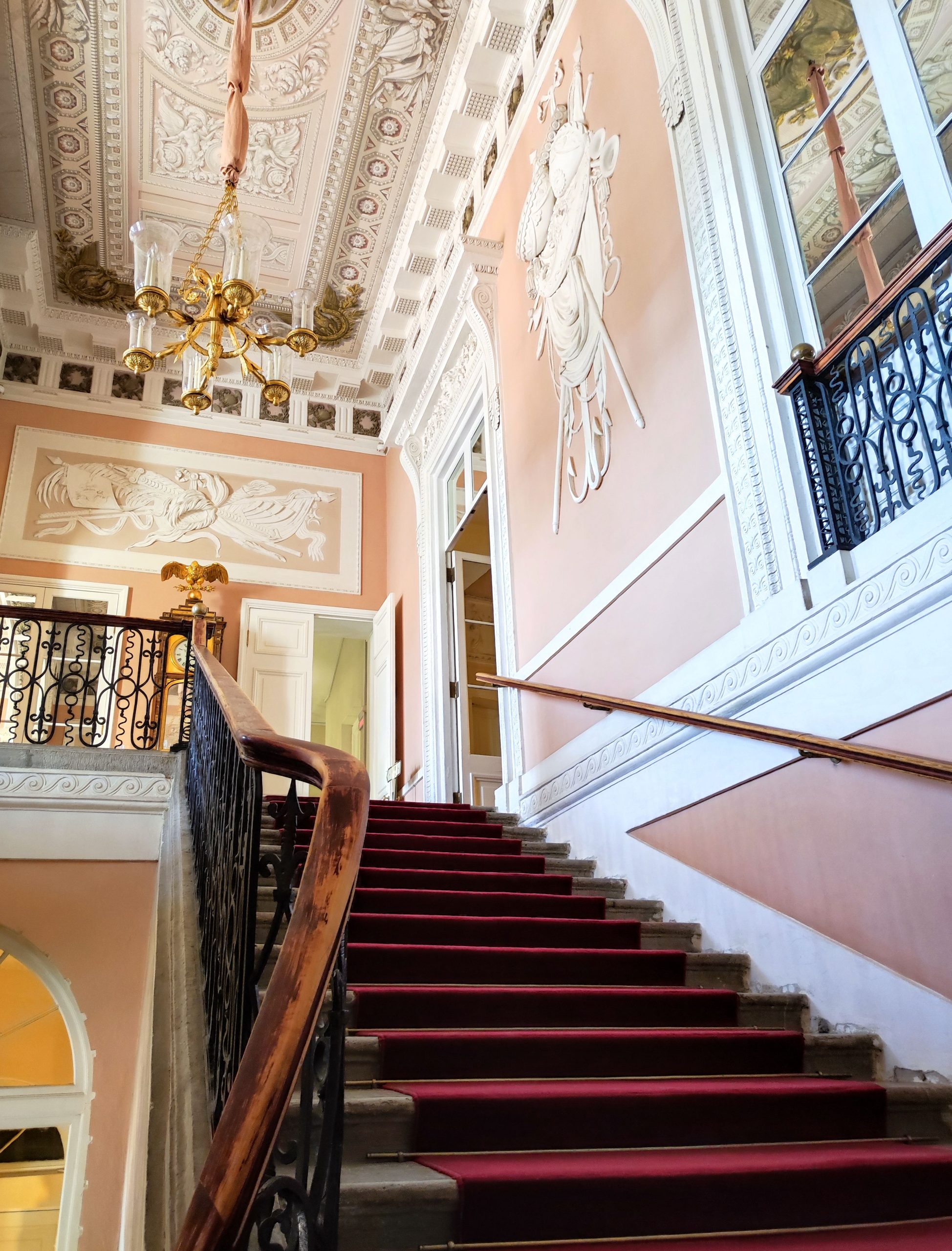 Intricate staircase and chandelier in a historical building, showcasing elegant architecture.