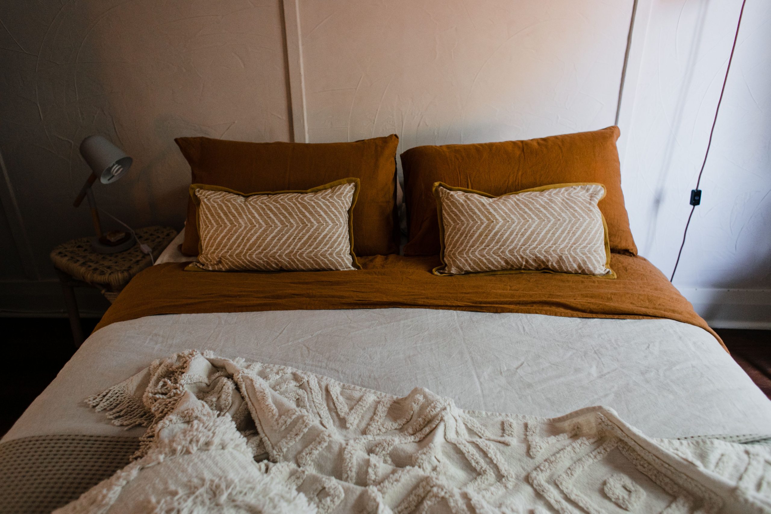 Inviting bedroom with warm tones, featuring a neatly arranged bed, pillows, and ambient lighting.
