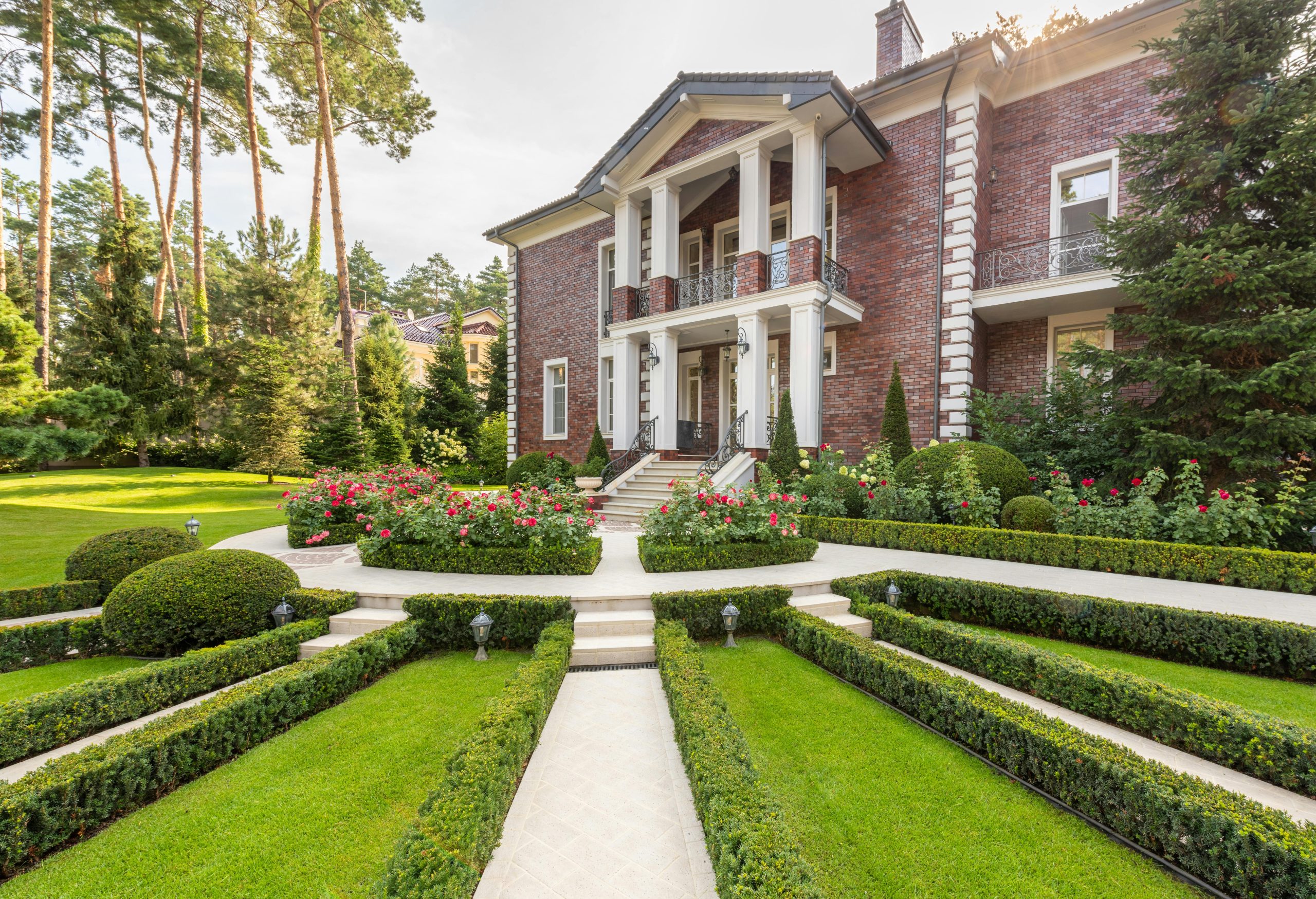 Modern house near backyard with green grass and plants near trees and path under sky in summer sunny day