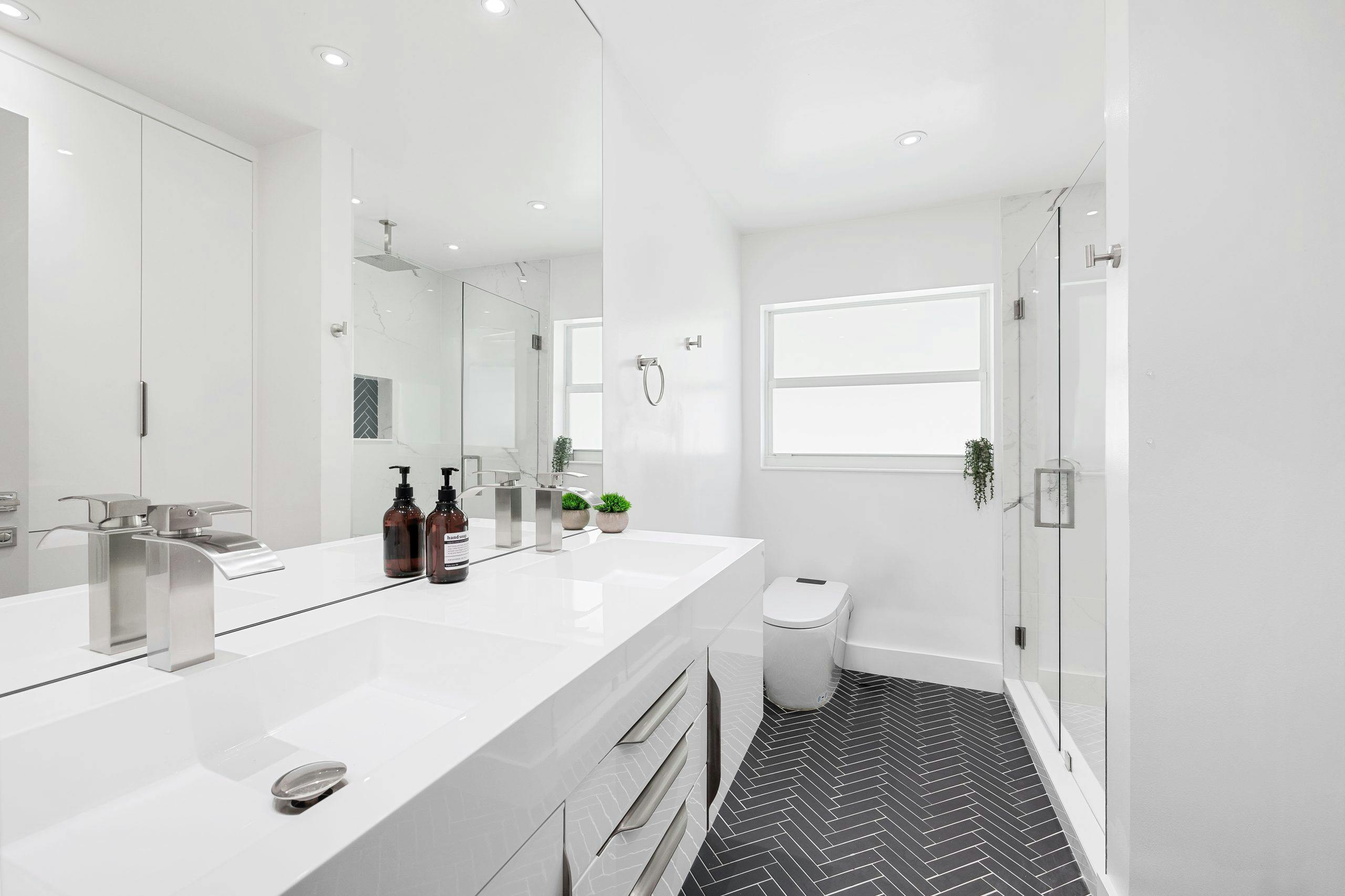 Modern white bathroom featuring sleek fixtures and herringbone flooring design.