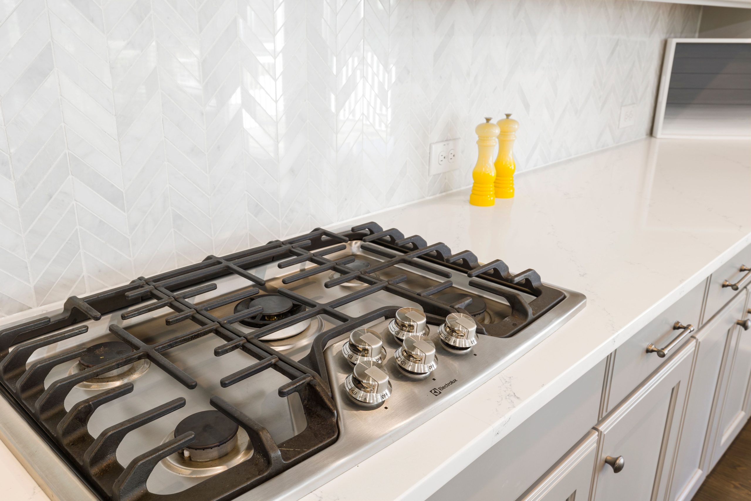 Sleek kitchen countertop featuring a gas stove and white tiled backsplash, with yellow salt and pepper shakers.