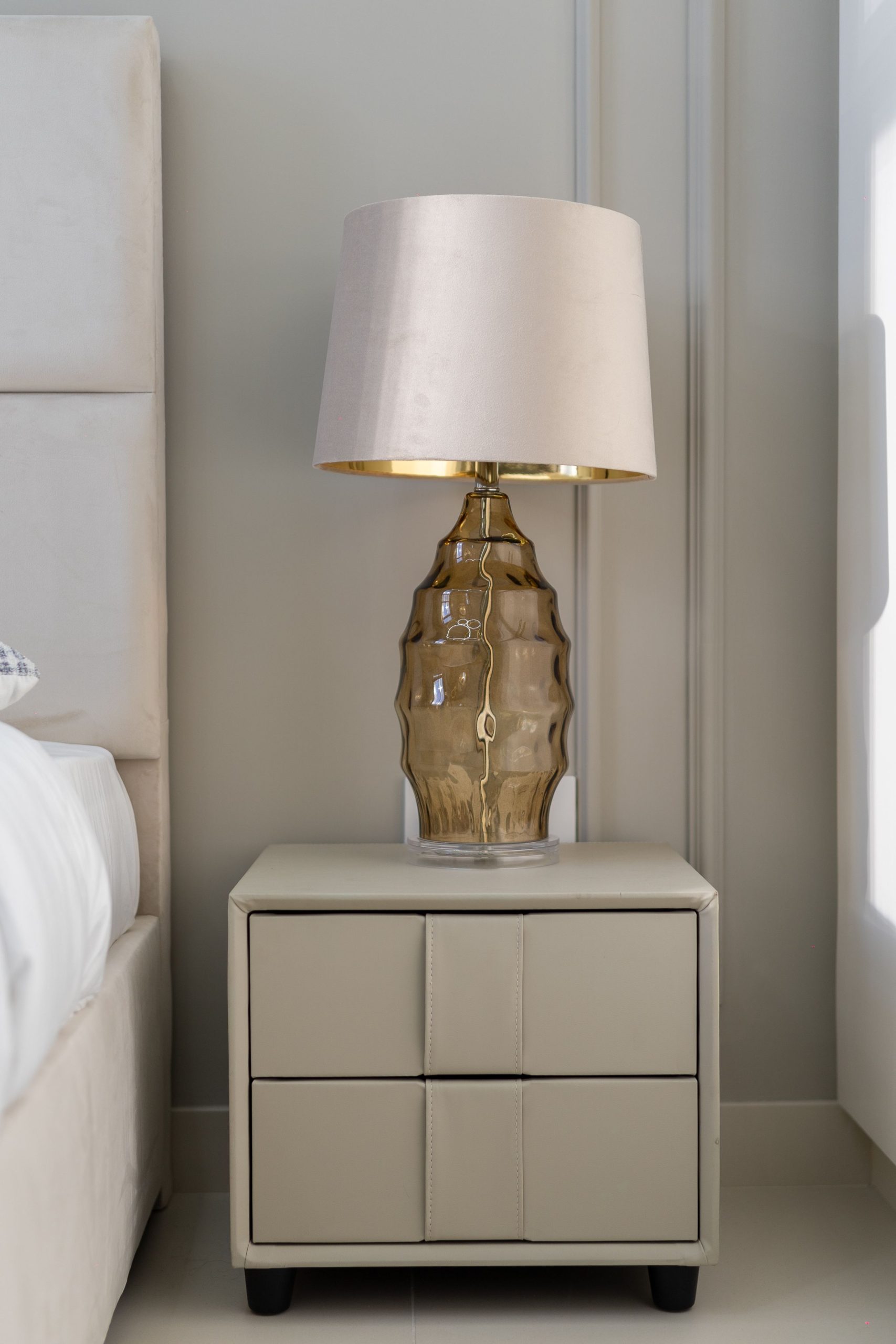 Sophisticated bedside table with a modern lamp in a sunlit bedroom setting.