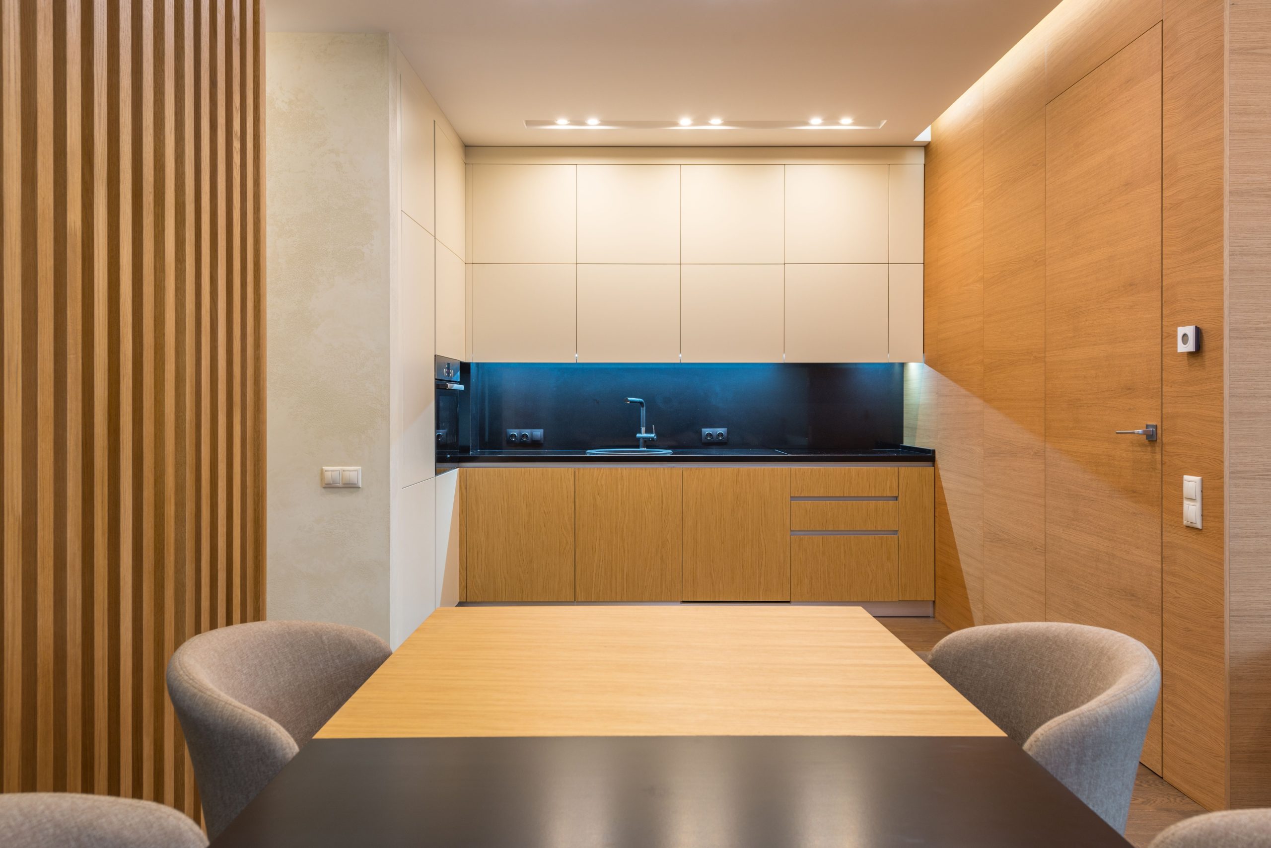 Spacious kitchen with illuminated cooking zone near wooden cabinets and soft chairs around table