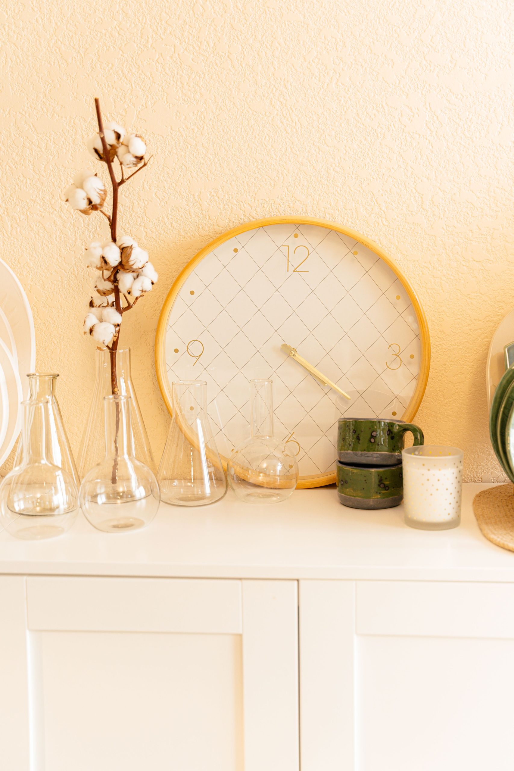 Stylish home interior featuring a decorative clock, cotton flowers, and glassware on a cabinet.