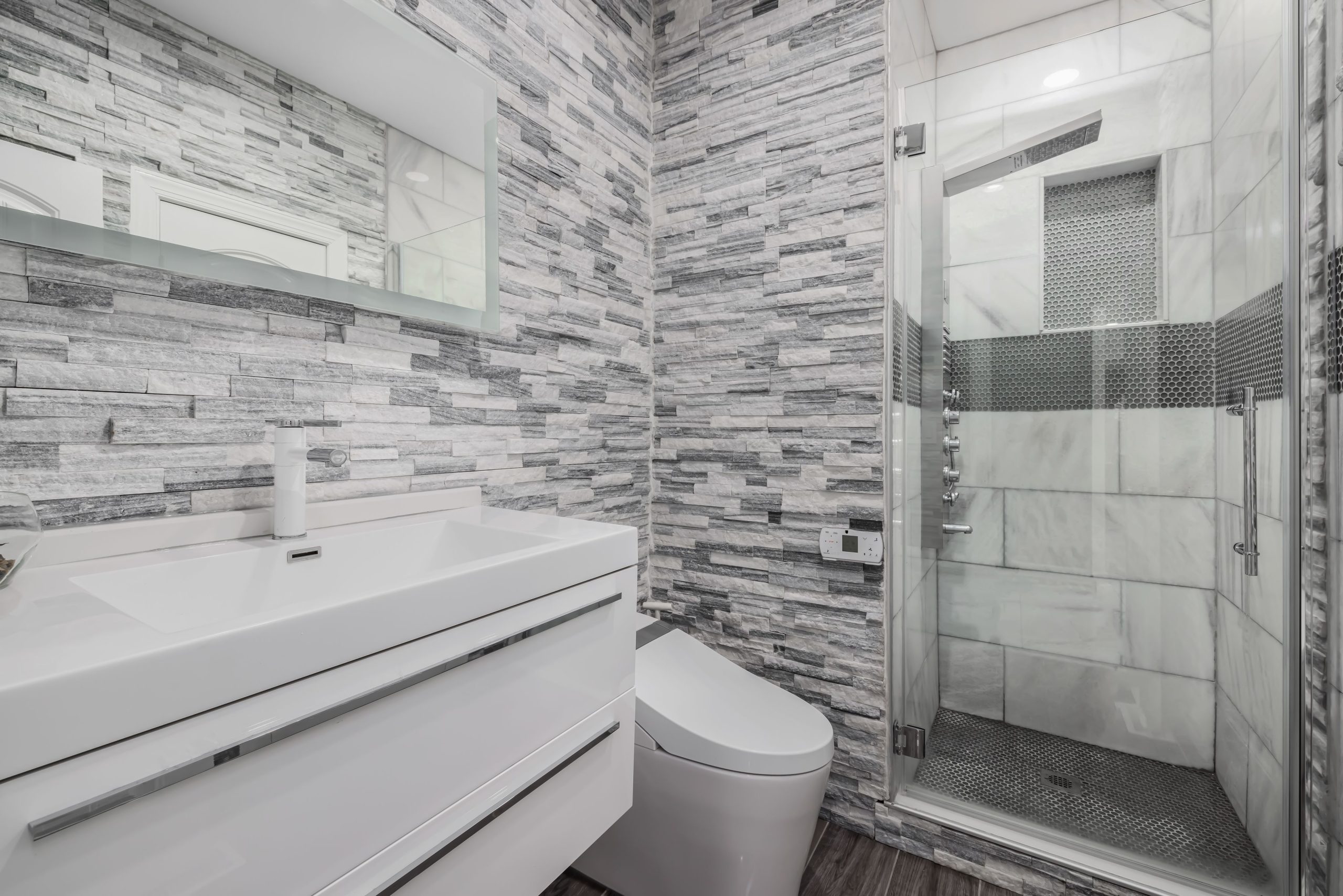 Stylish modern bathroom featuring a glass shower, stone walls, and sleek white vanity.