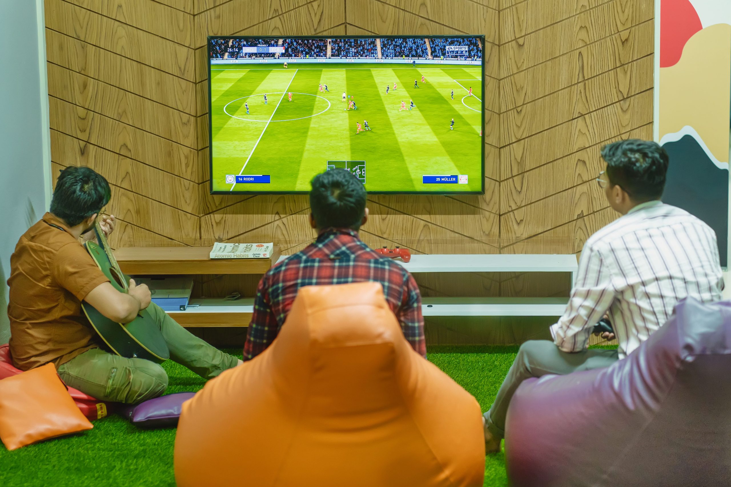 Three friends relaxing and playing a soccer video game indoors on a comfortable game night.