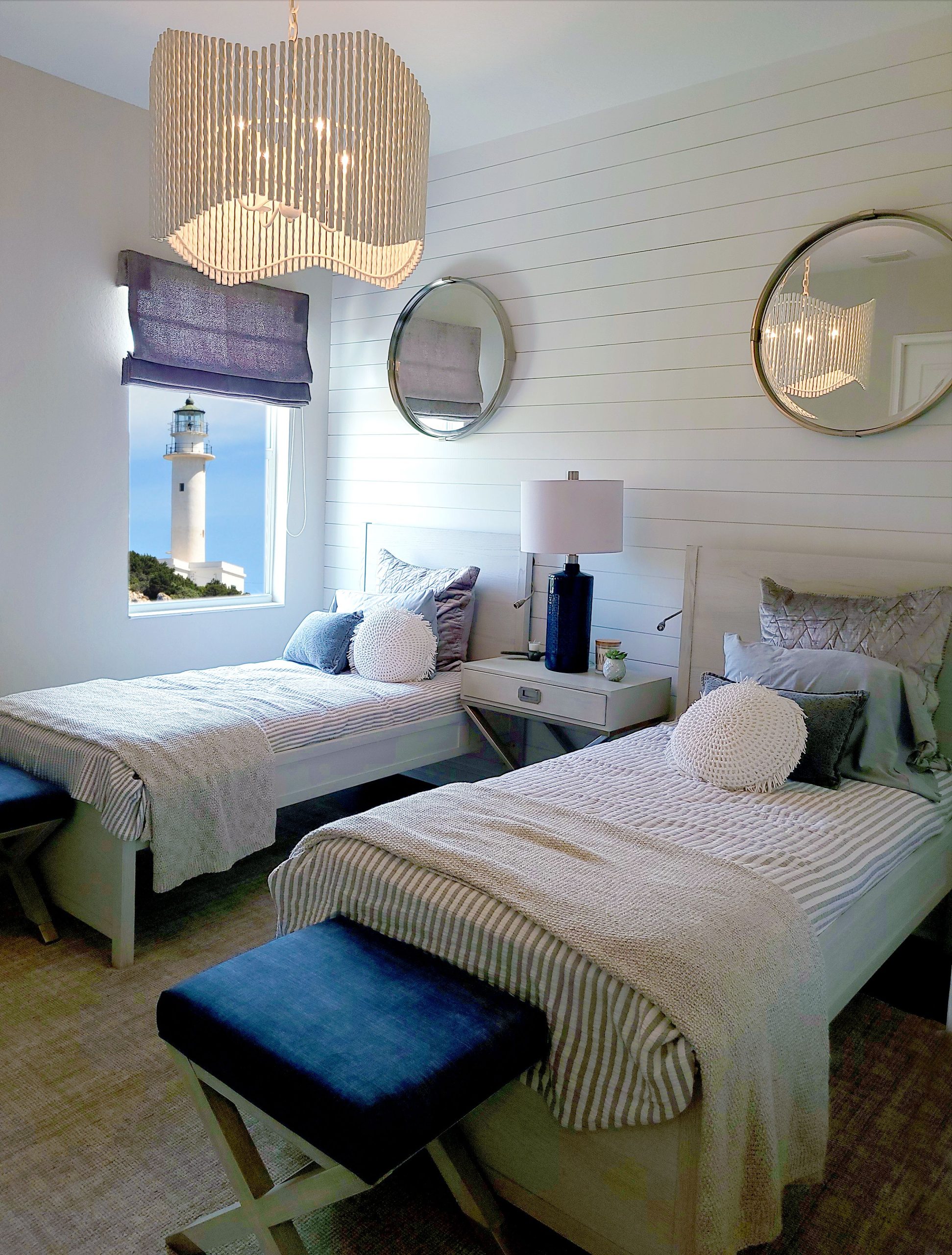 Twin beds in a coastal-themed room with lighthouse view through window, showcasing elegant decor.