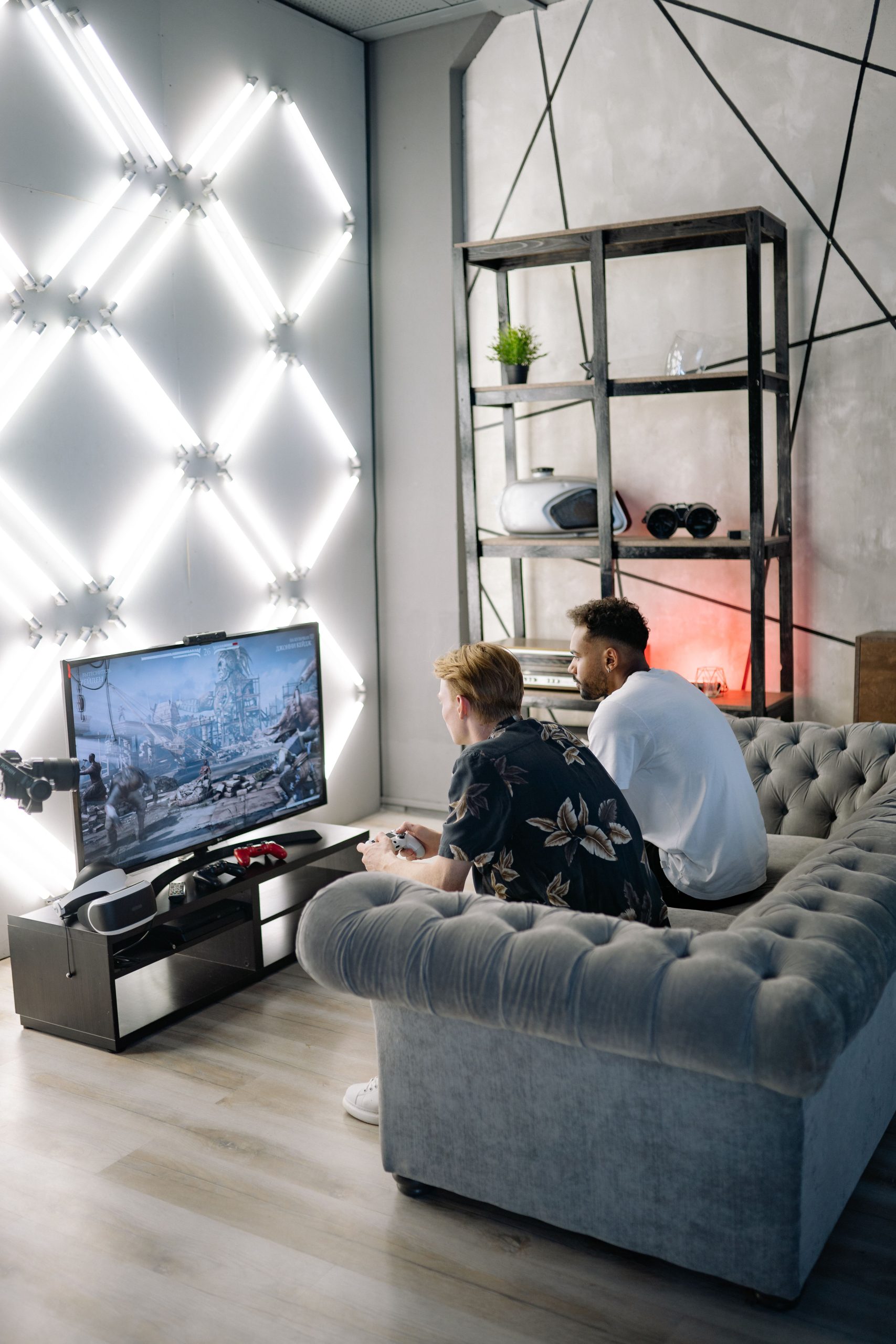 Two friends enjoy playing video games in a stylish, modern apartment setting with unique lighting.