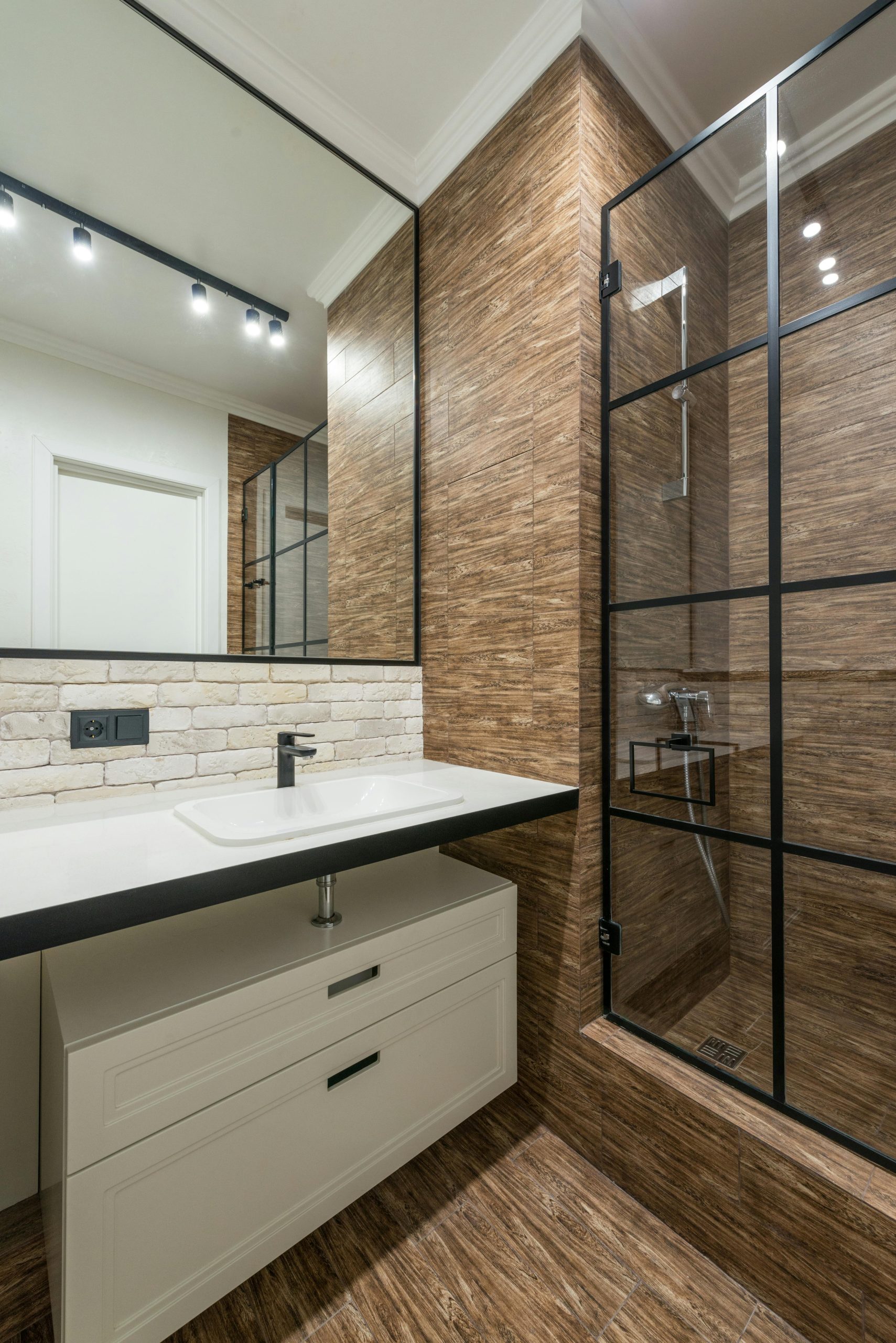 White cabinet under sink at wall with mirror near glass shower cabin in modern stylish bathroom with glowing lights in apartment