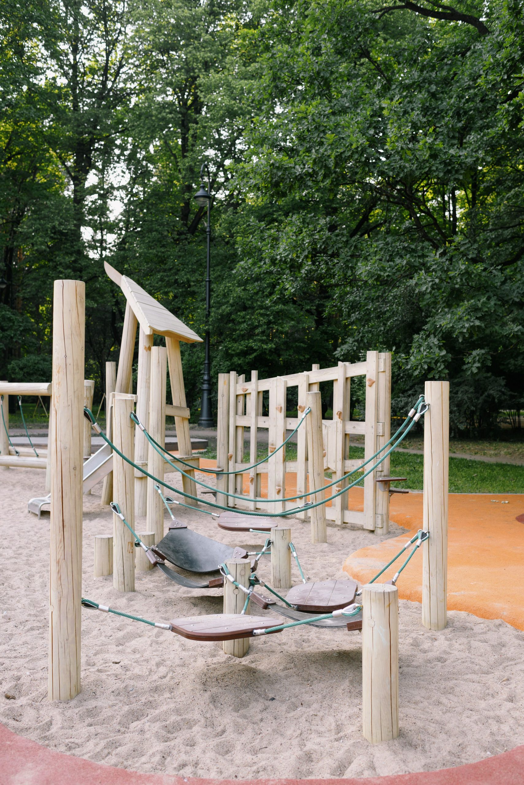 Wooden playground equipment with ropes and sand, set in a lush green park.