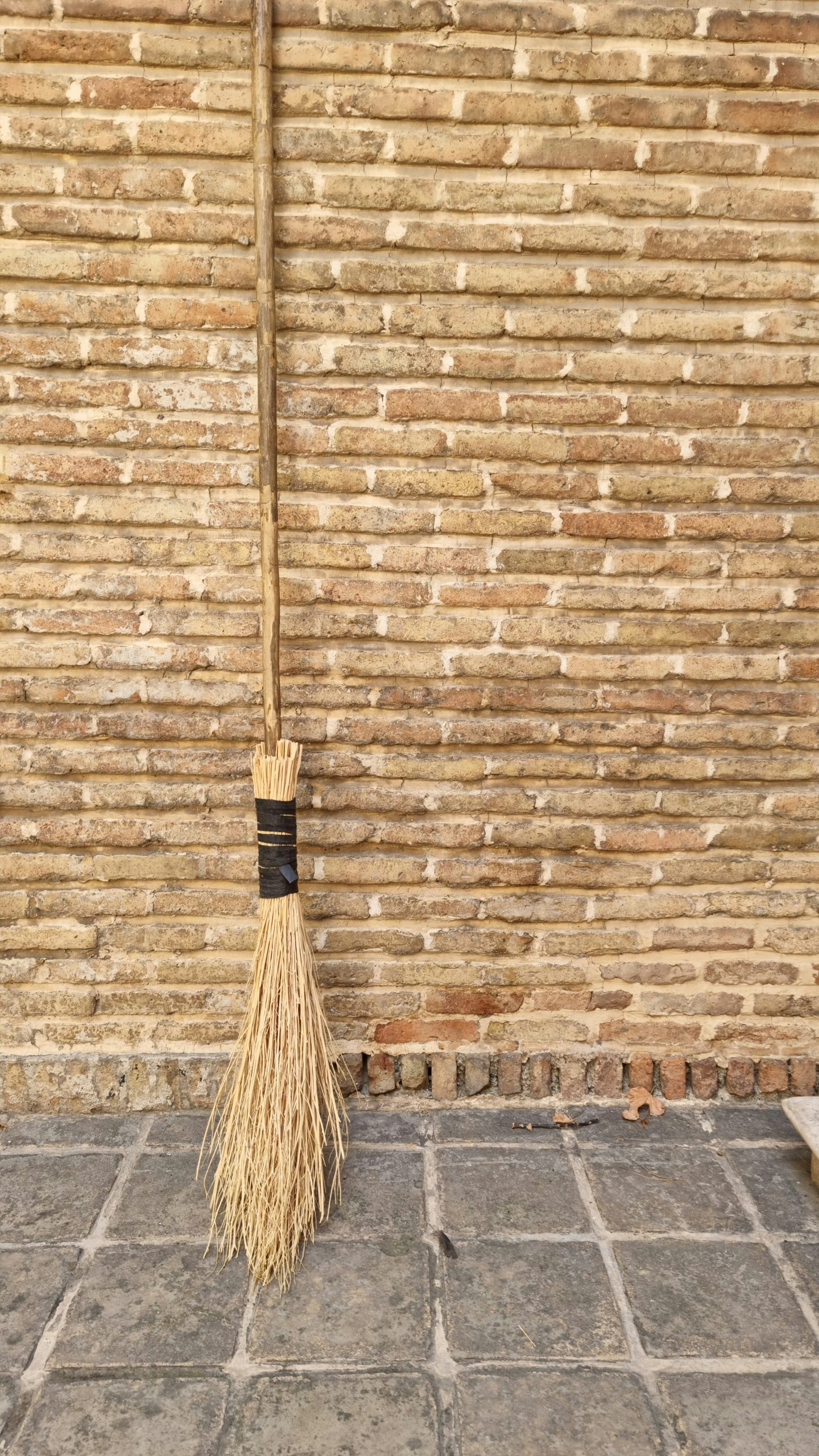 A broom leaning against a brick wall