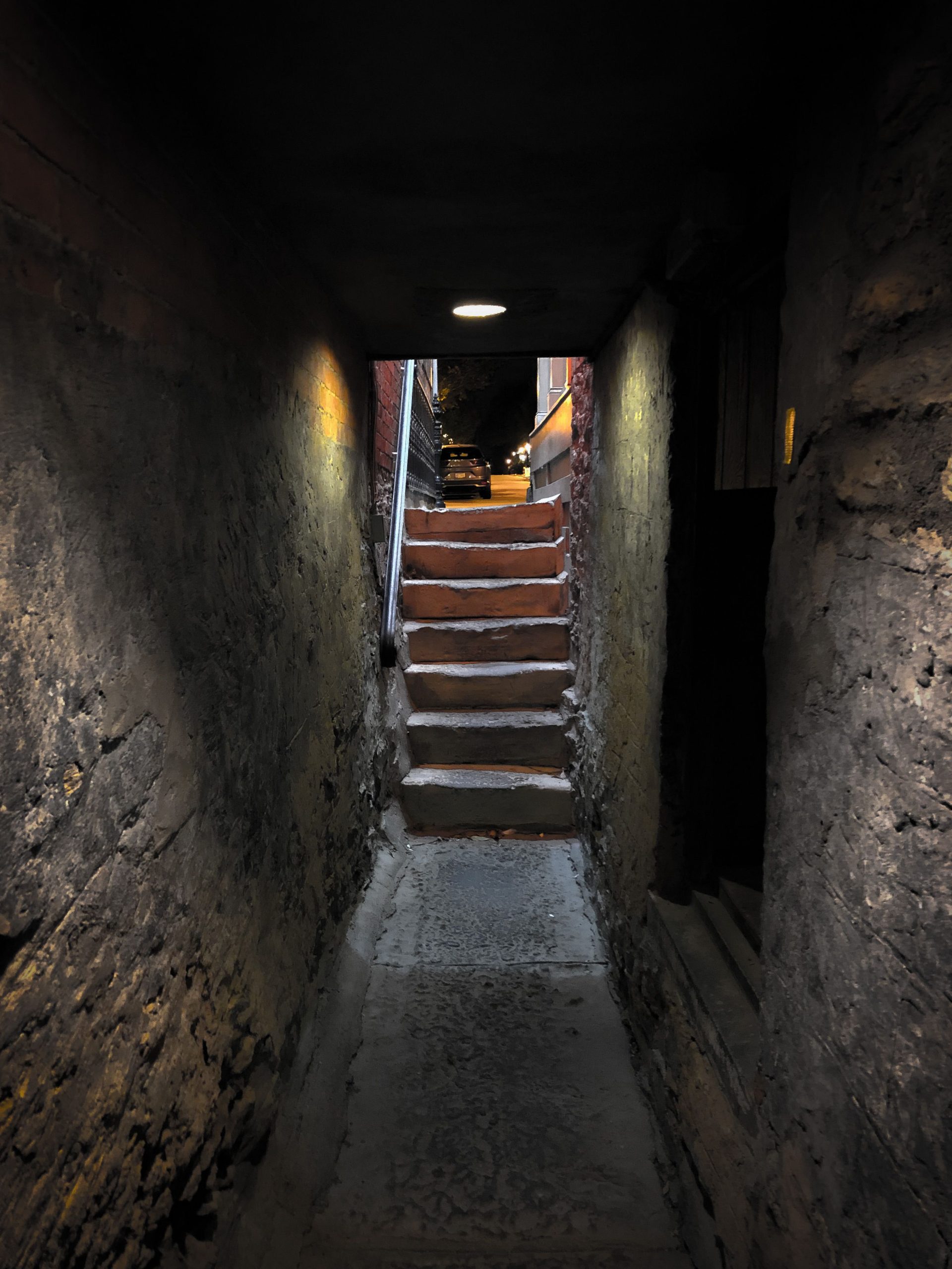 A dimly lit passageway in a narrow basement with steps leading upward.