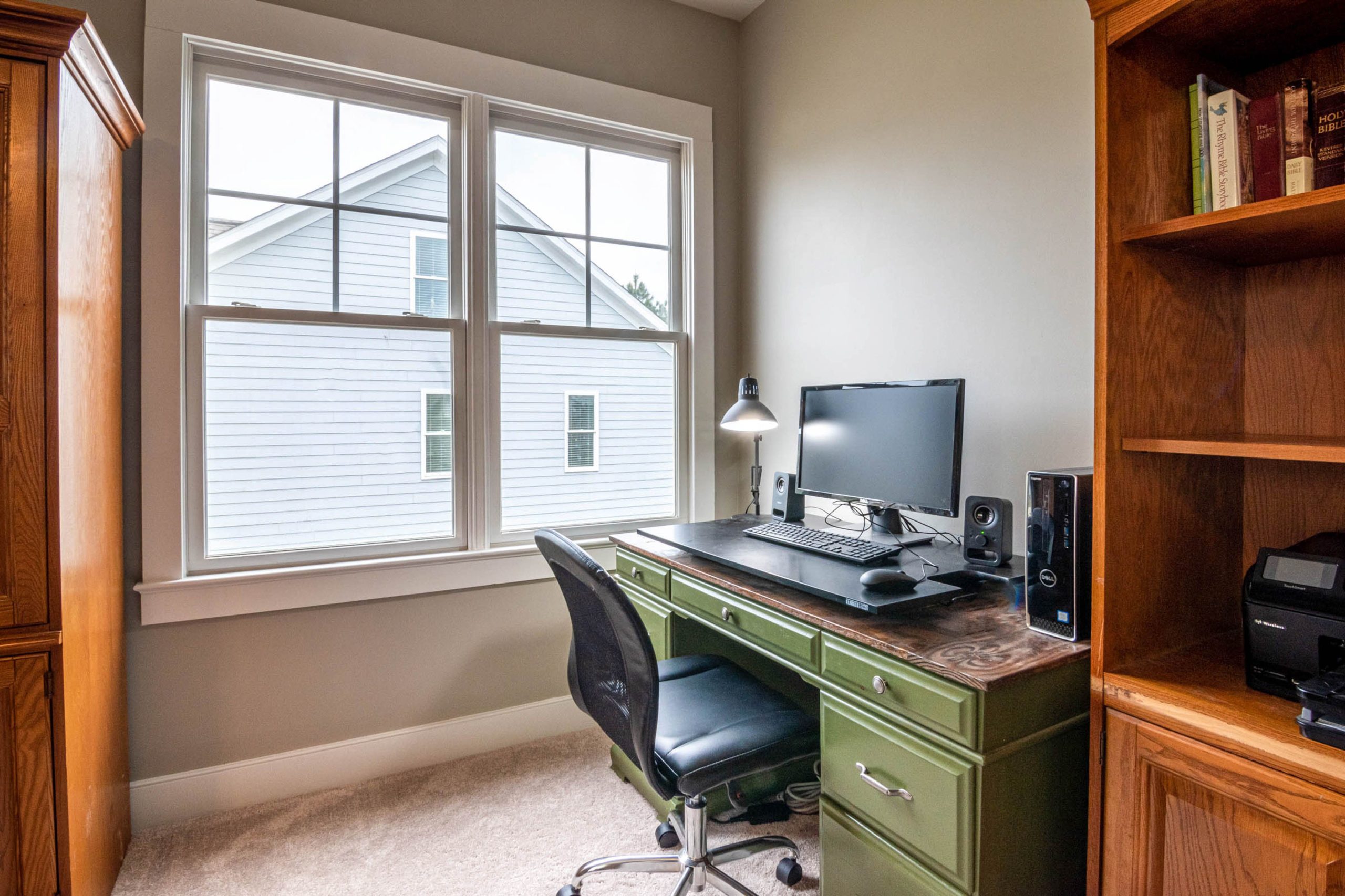 A neat and cozy home office setup with a desk, monitor, and window view.